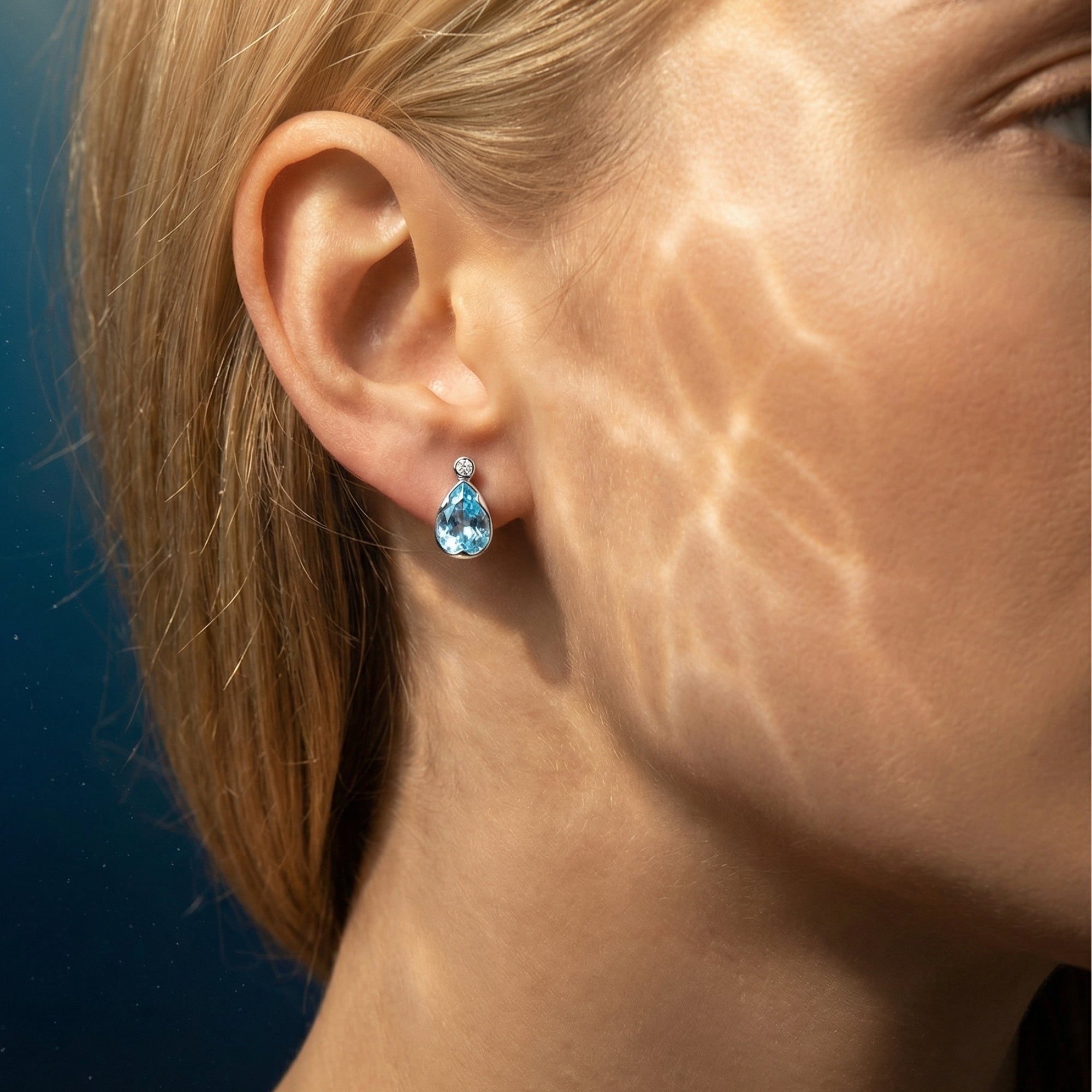 Side view of a pear cut aquamarine drop earring in platinum worn on a model's ear with soft light reflections.