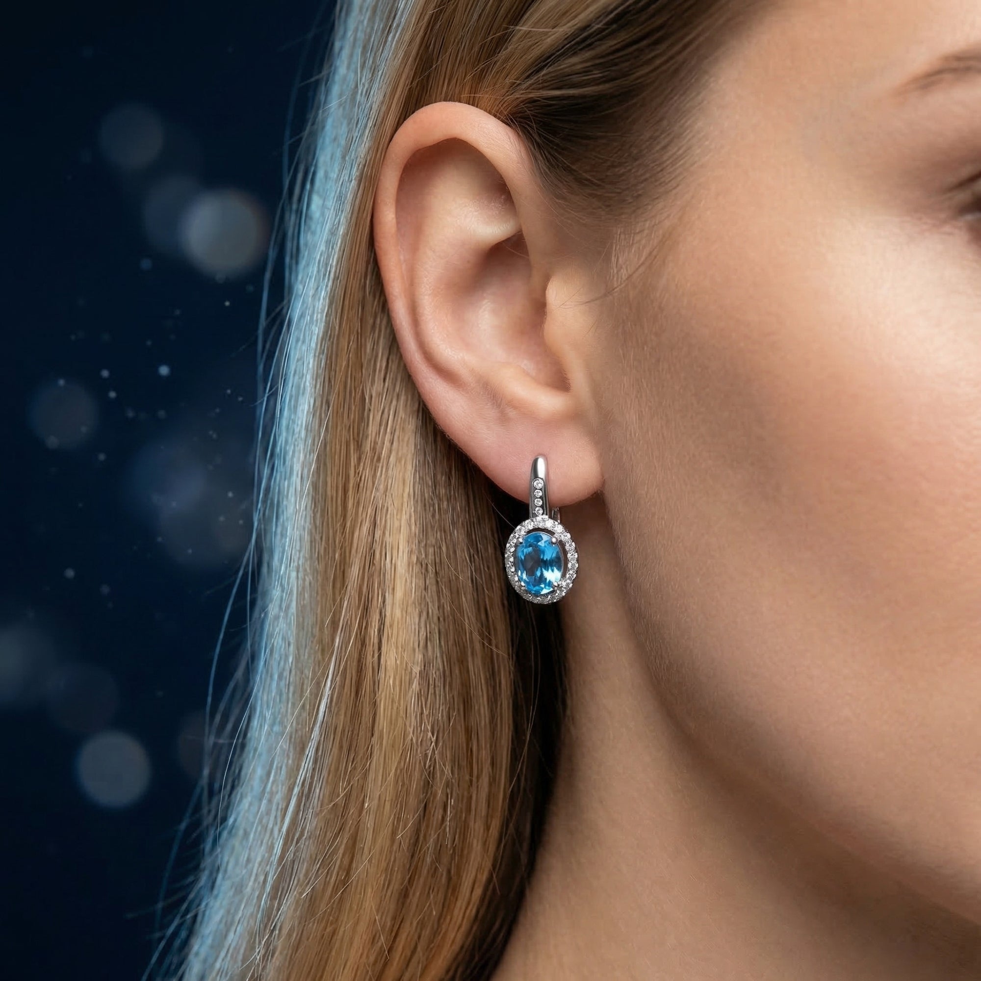 Side view of a silver drop earring with an oval Swiss blue topaz and halo setting, worn on a woman's ear.