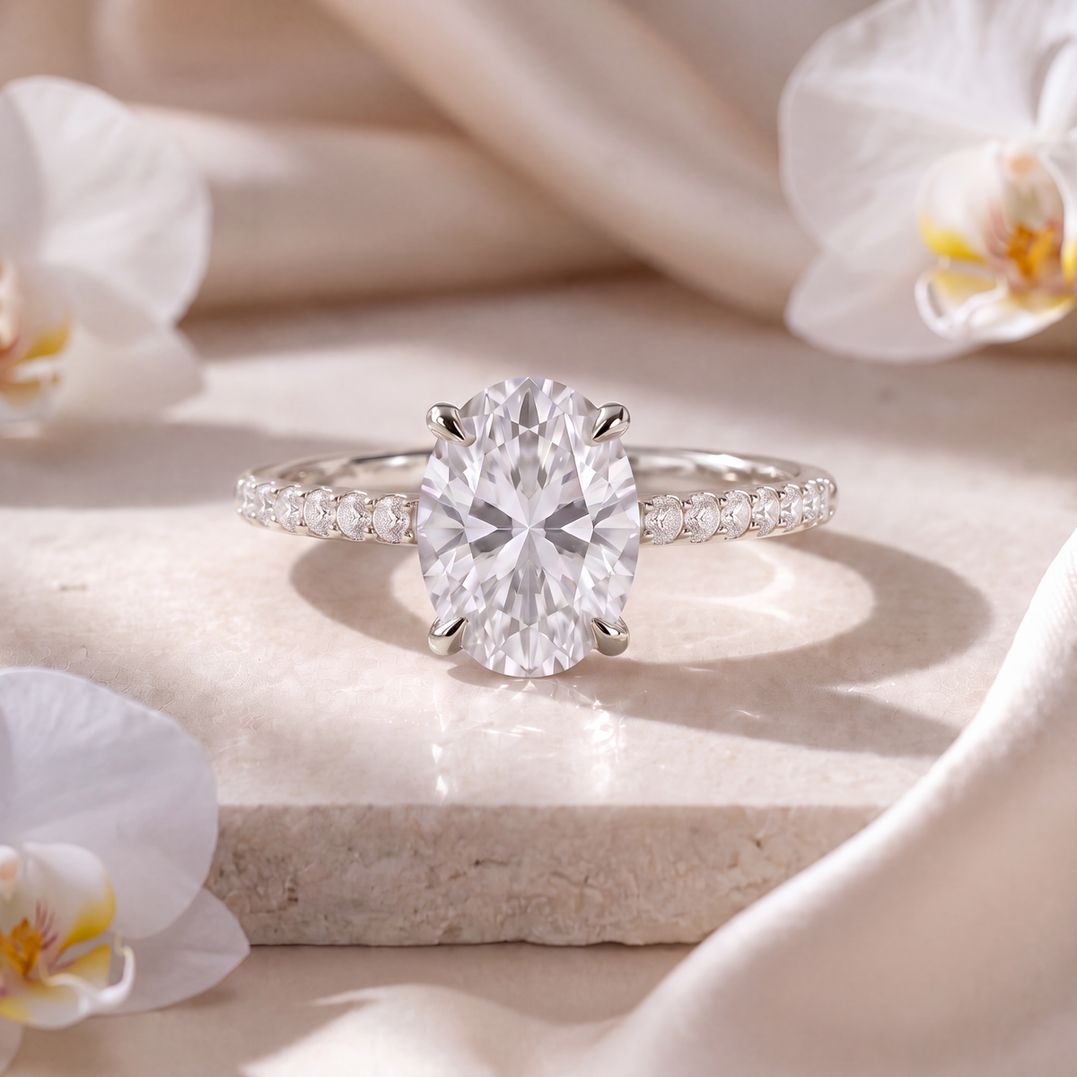 White gold oval-cut moissanite engagement ring with a pavé band resting on a marble pedestal.