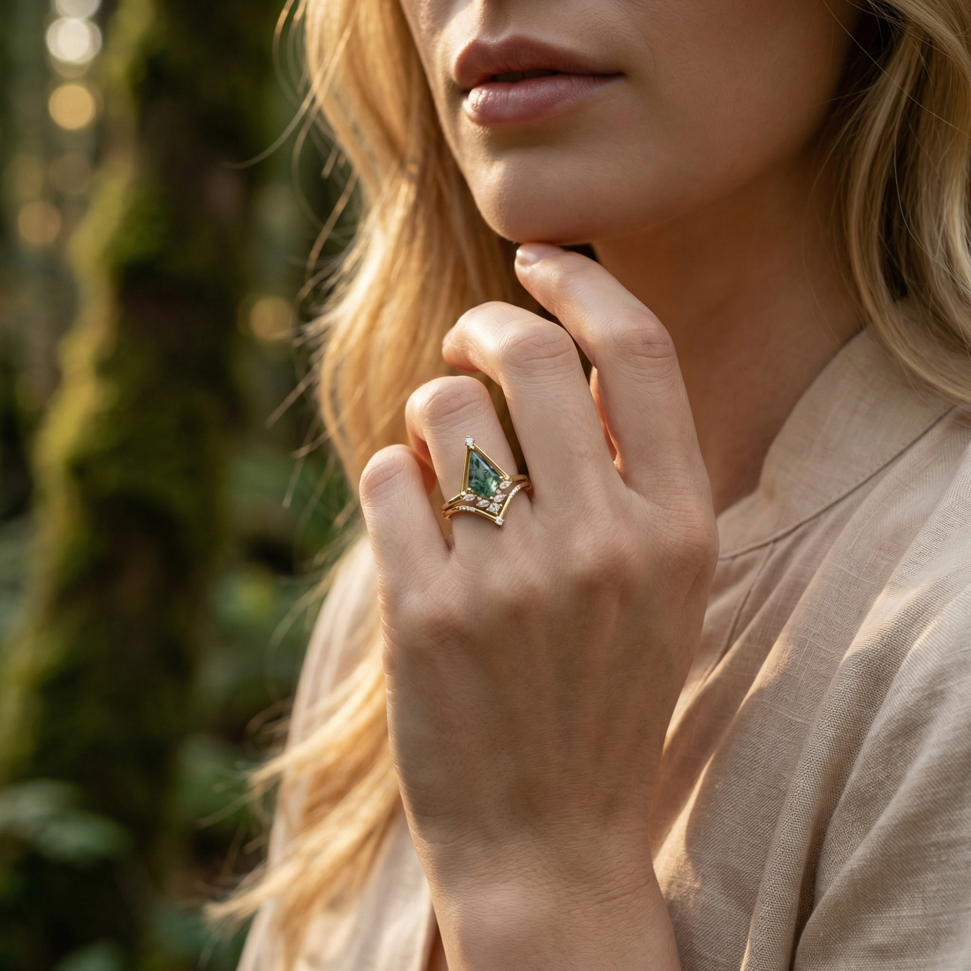 Close-up of a woman's hand wearing the triangular moss agate and diamond accent ring set outdoors.