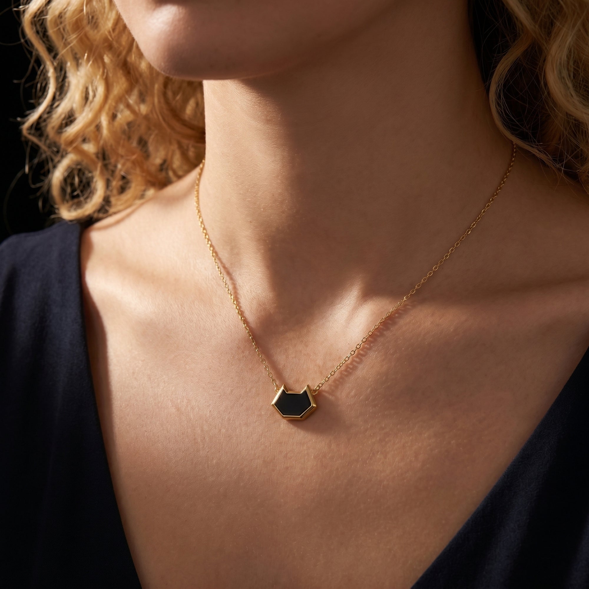 Model wearing the Umbra irregular-cut black onyx pendant necklace in 18K gold plating against a black V-neck top.