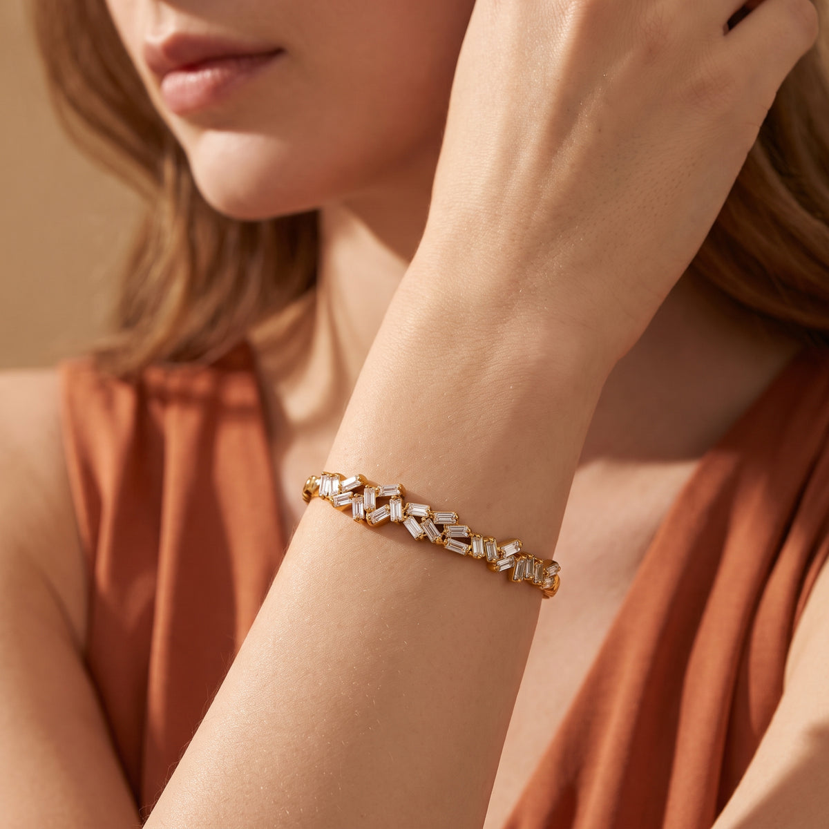 Model in a rust-colored dress wearing the gold-tone baguette zigzag cuff bracelet on her wrist.