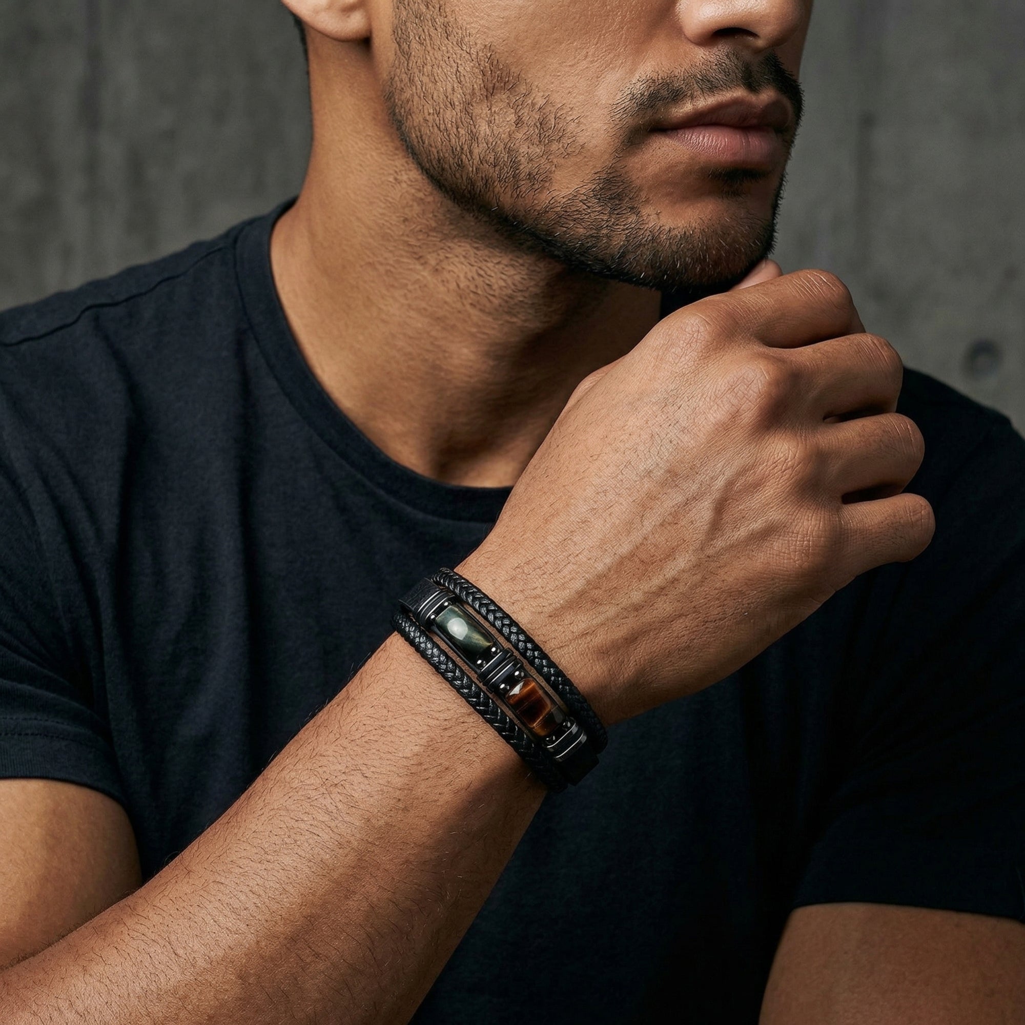 Model wearing a men's black braided leather bracelet with tiger's eye cabochon stones and black stainless steel hardware.