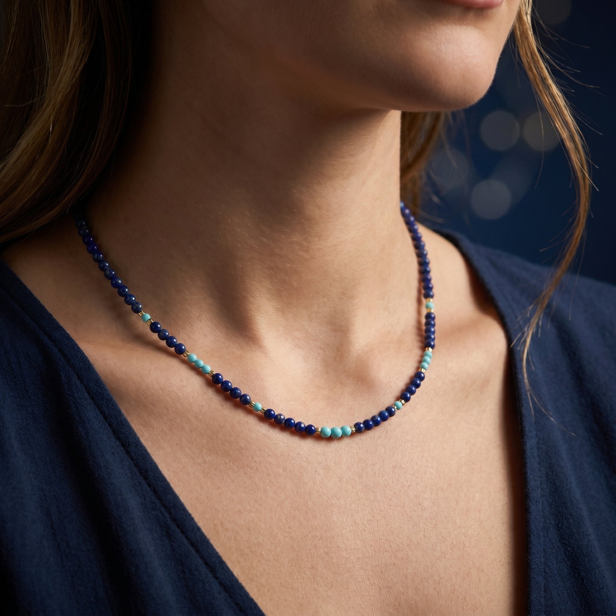 Close-up of a model wearing a natural lapis lazuli bead necklace with light blue accents and gold plated beads.