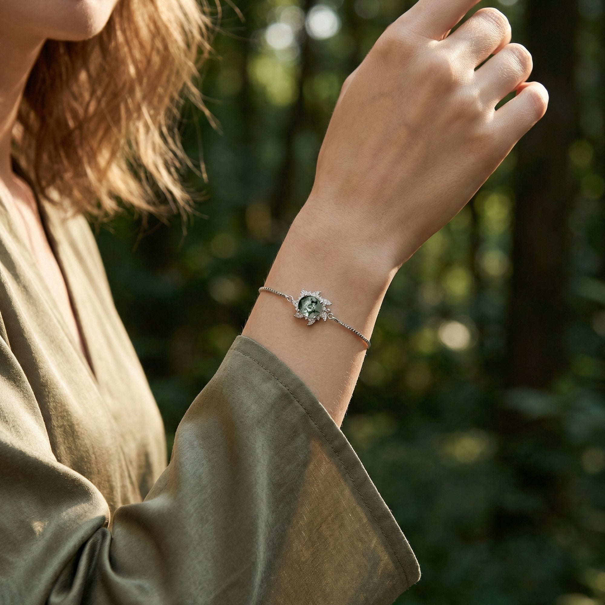 Sunburst moss agate bracelet in S925 sterling silver worn on a wrist against a blurred forest background.