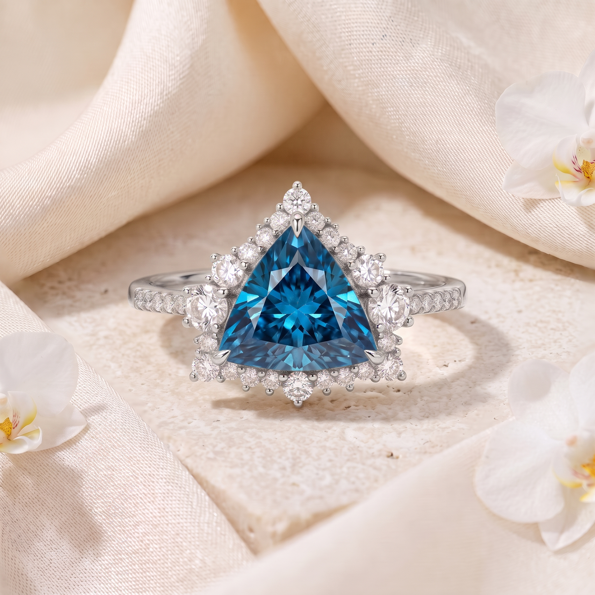Trillion-cut blue moissanite halo engagement ring in white gold displayed on stone with silk fabric.