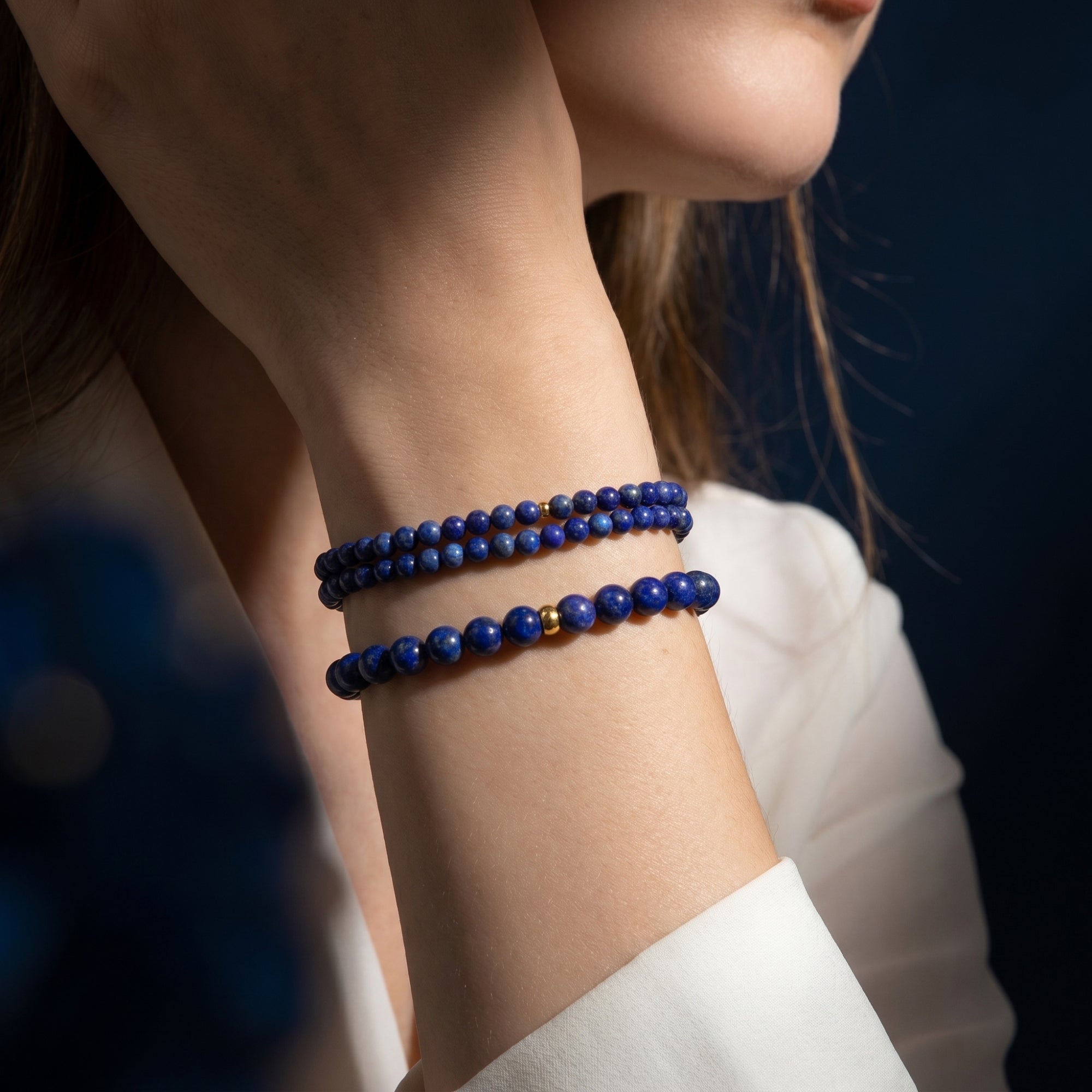 A stack of three natural lapis lazuli beaded bracelets with gold spacers styled on a model's wrist.
