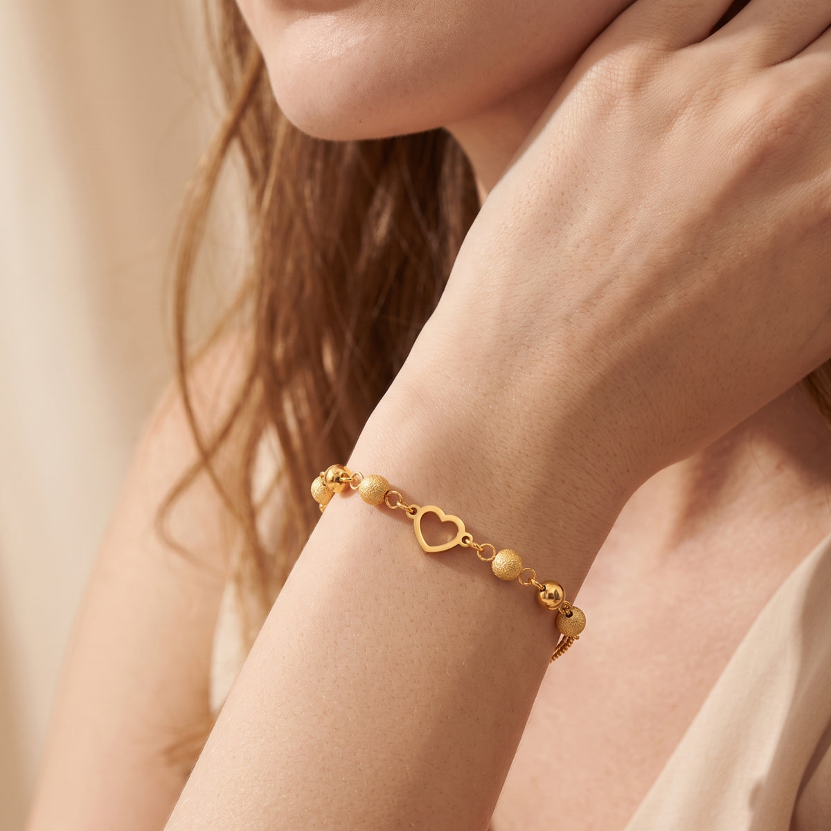 Close-up of the gold-tone heart bracelet worn on a wrist, with the heart centerpiece and textured beads visible.