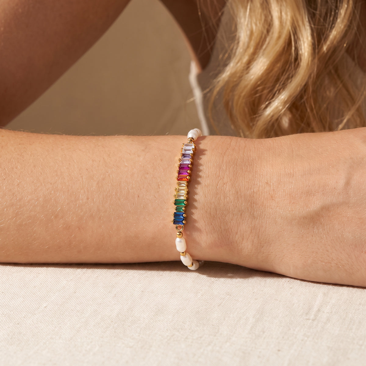 Gold-tone rainbow baguette and pearl bracelet worn across a horizontal forearm.