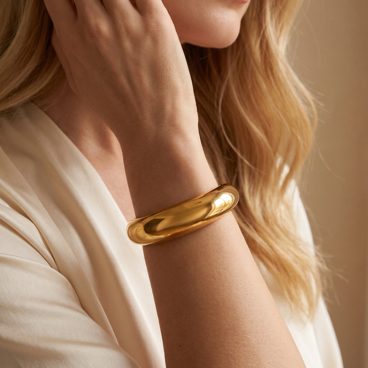 Close-up side view of the chunky gold-toned dome cuff bracelet worn on a model's wrist.