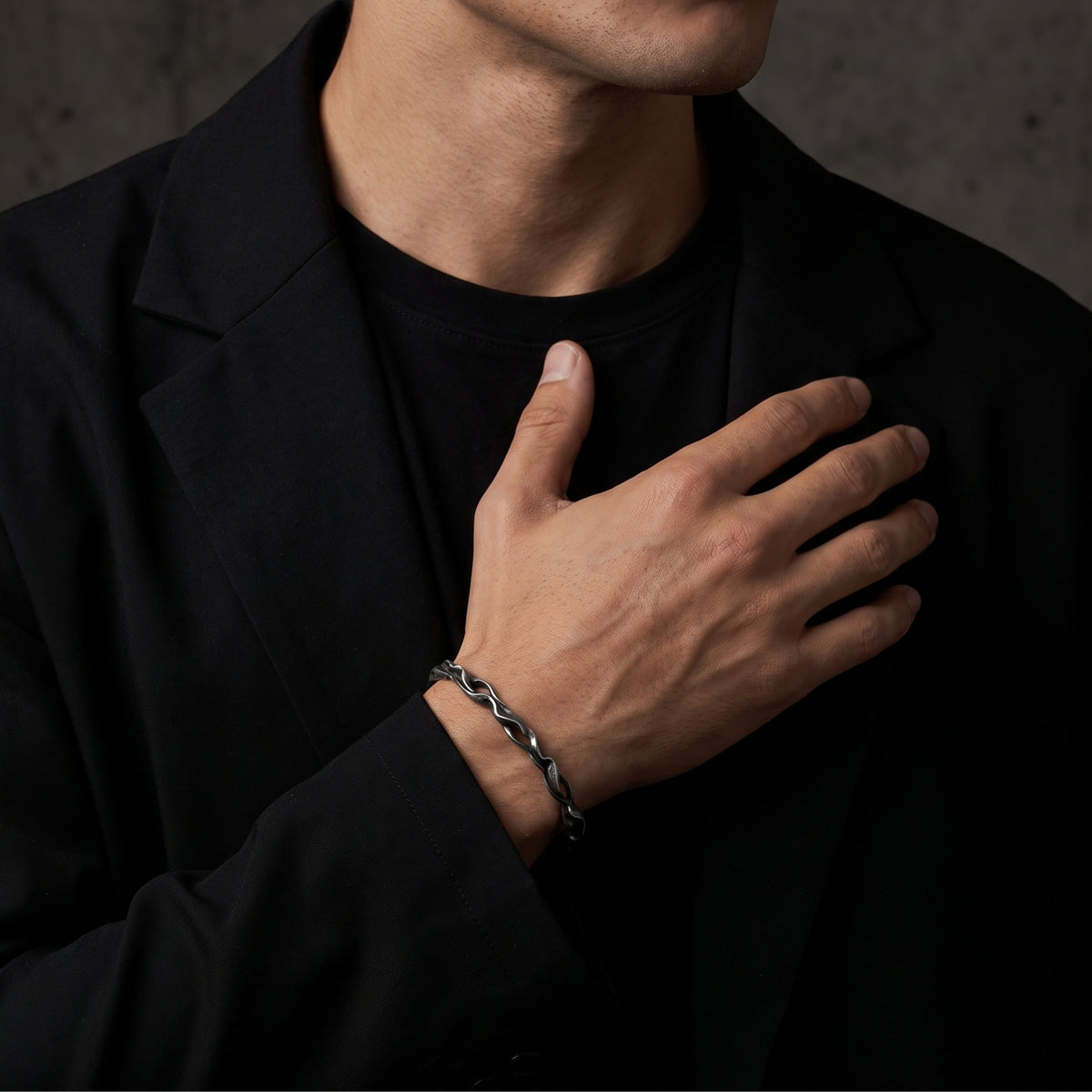 Model in a black blazer with one hand on his chest, wearing the silver wave cuff bracelet.