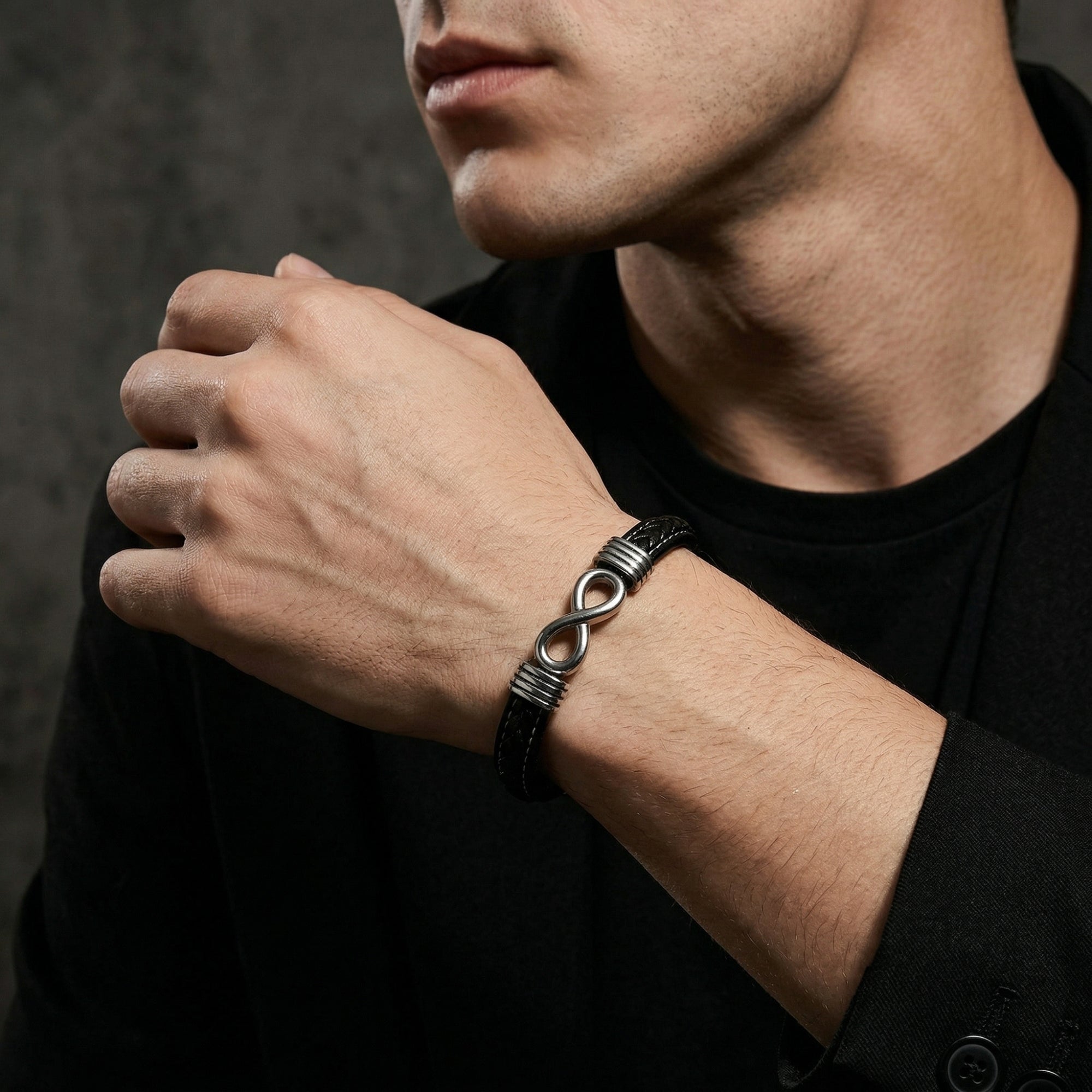 Men's black braided leather bracelet with a silver stainless steel infinity clasp, styled on a man's wrist.