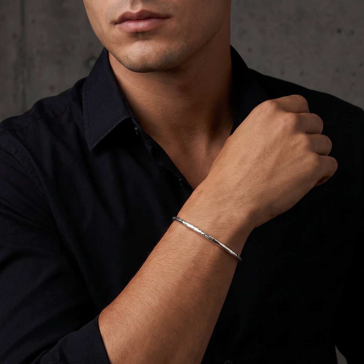 Torso view of a model in a black shirt wearing the hammered silver open cuff bracelet.