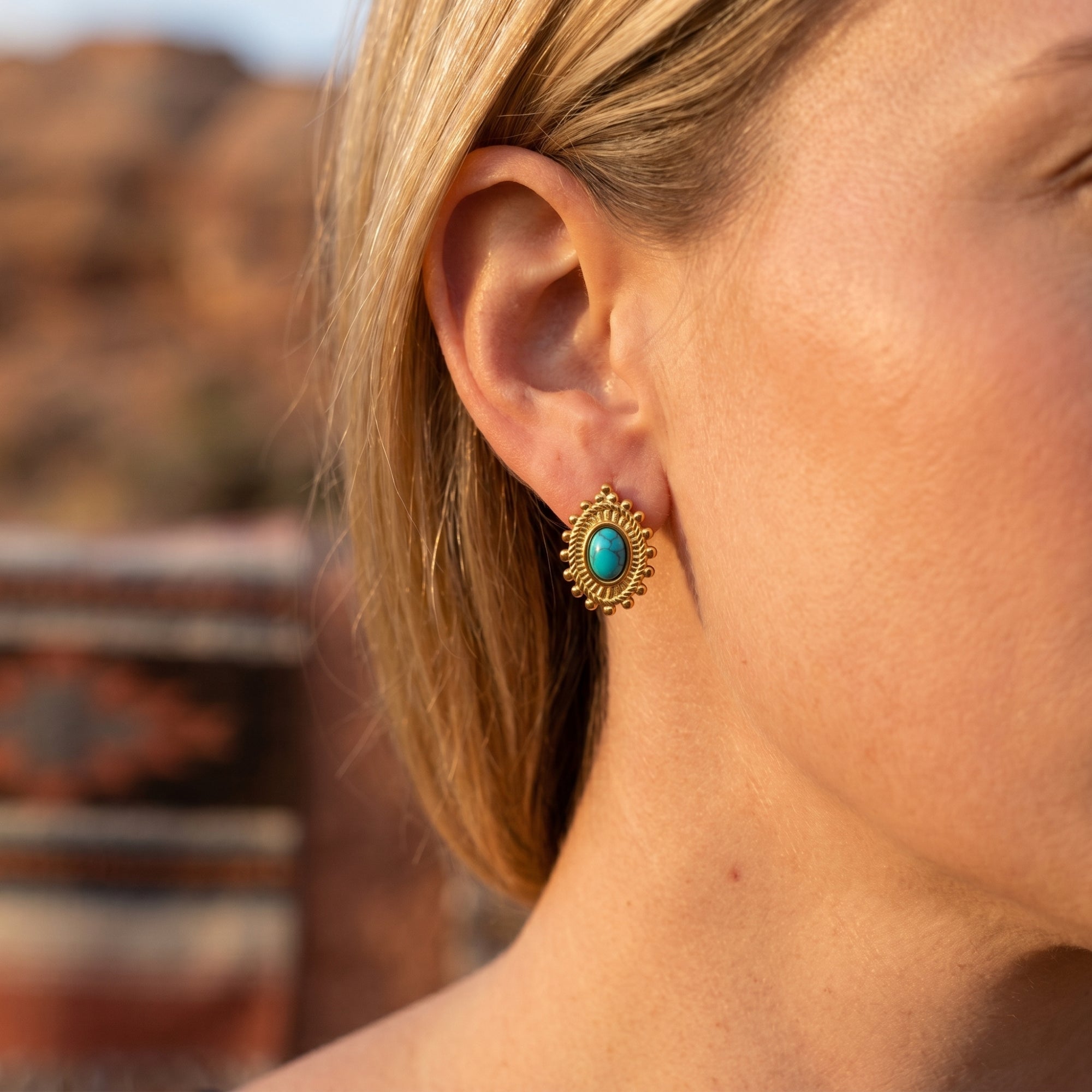 Close-up of a gold-tone drop earring with a turquoise-hued oval cabochon worn on a model's ear.