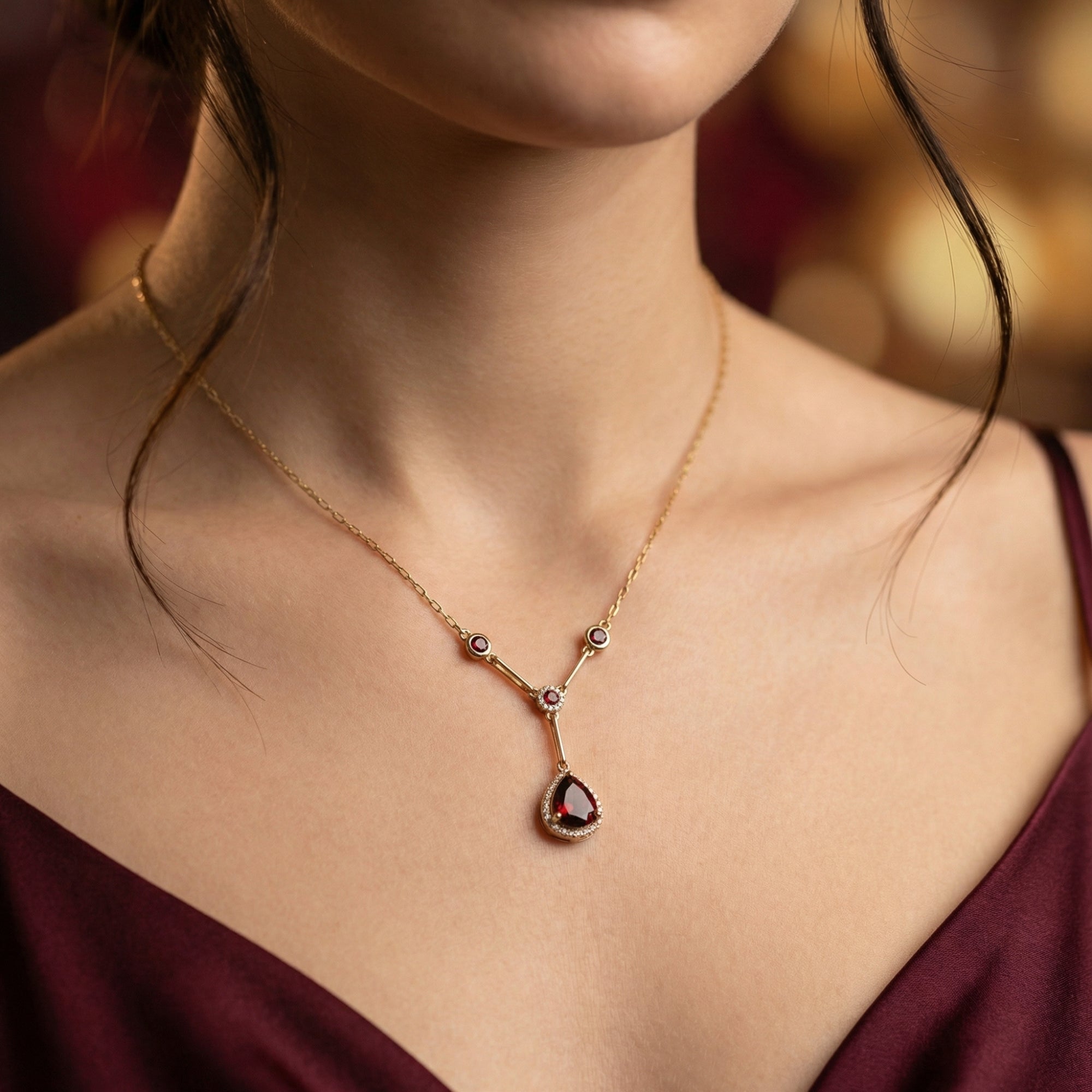 18K yellow gold Y-shaped necklace with a pear cut garnet pendant worn by a model.