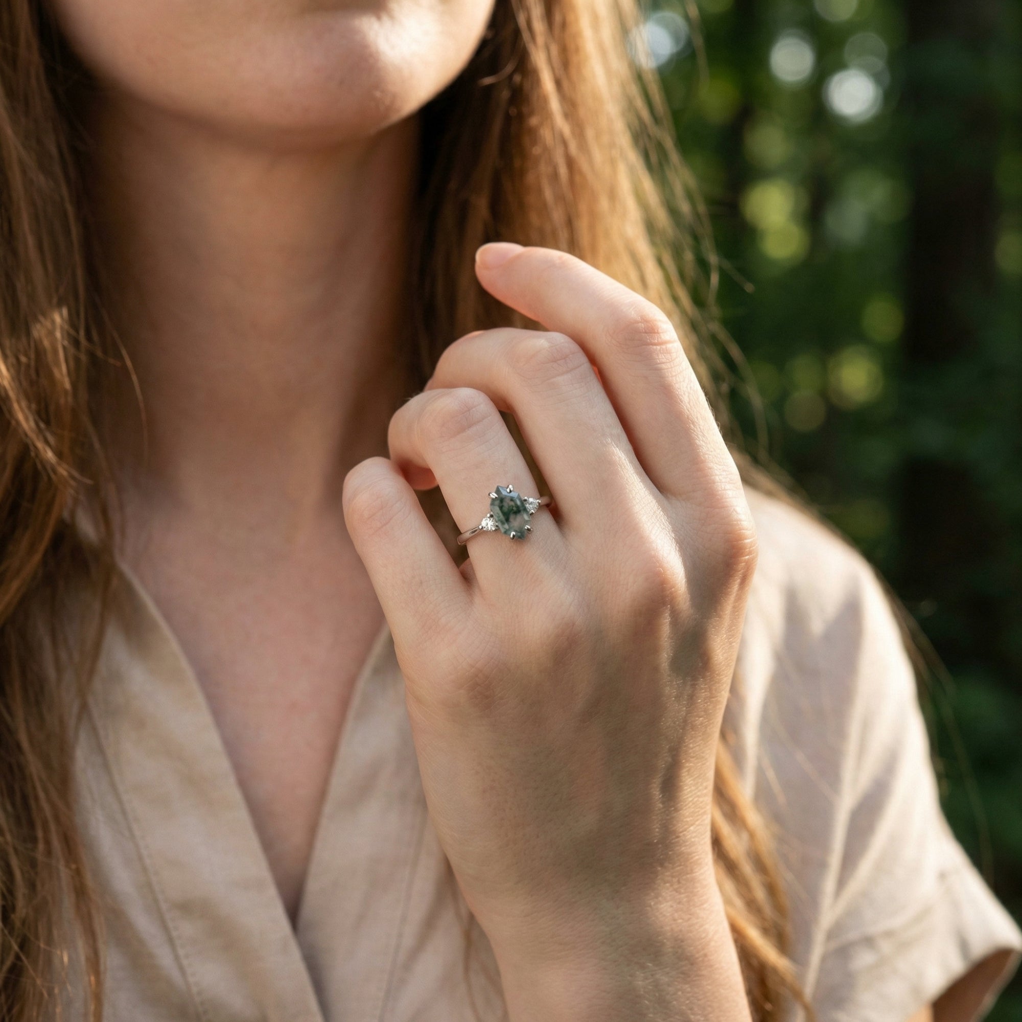 Sterling silver moss agate ring worn on a model's hand with a blurred nature background.
