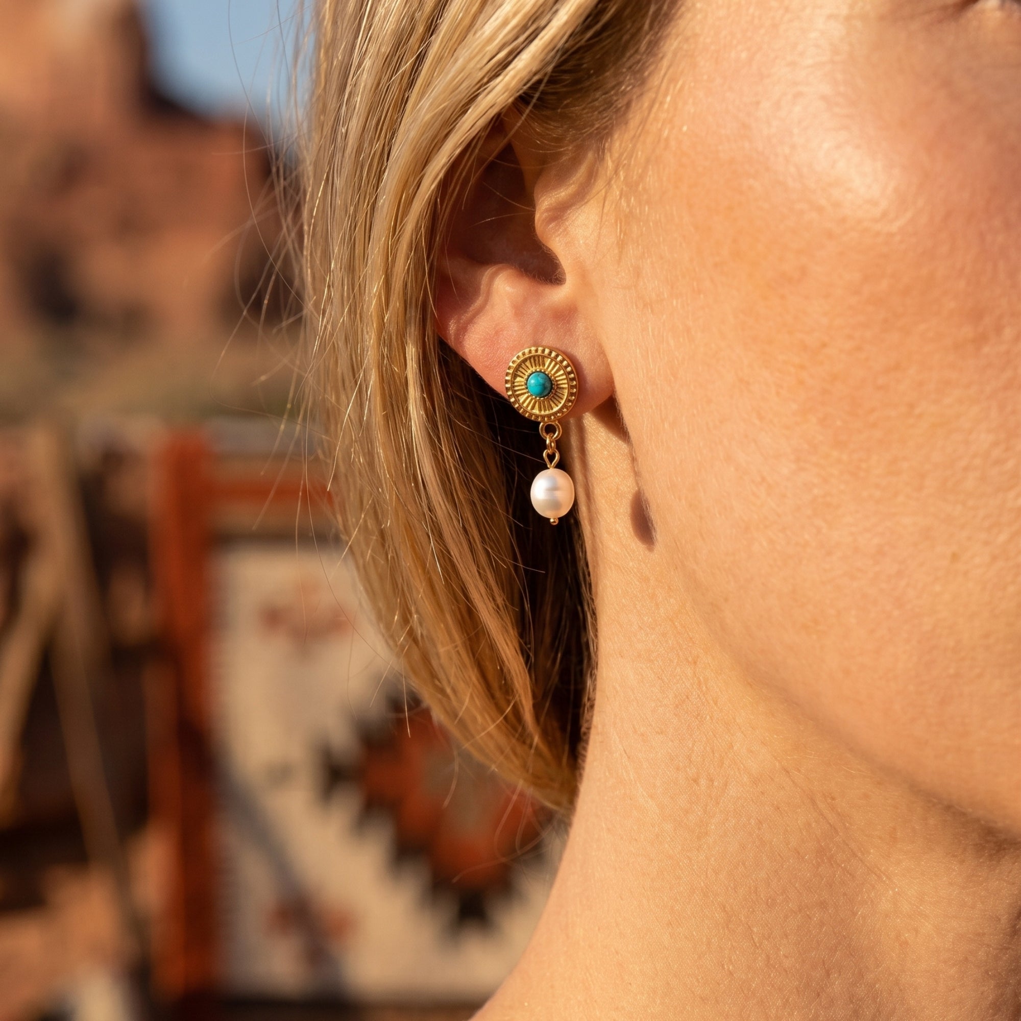 Model wearing gold Southwestern-style turquoise and pearl drop earrings with a desert background.