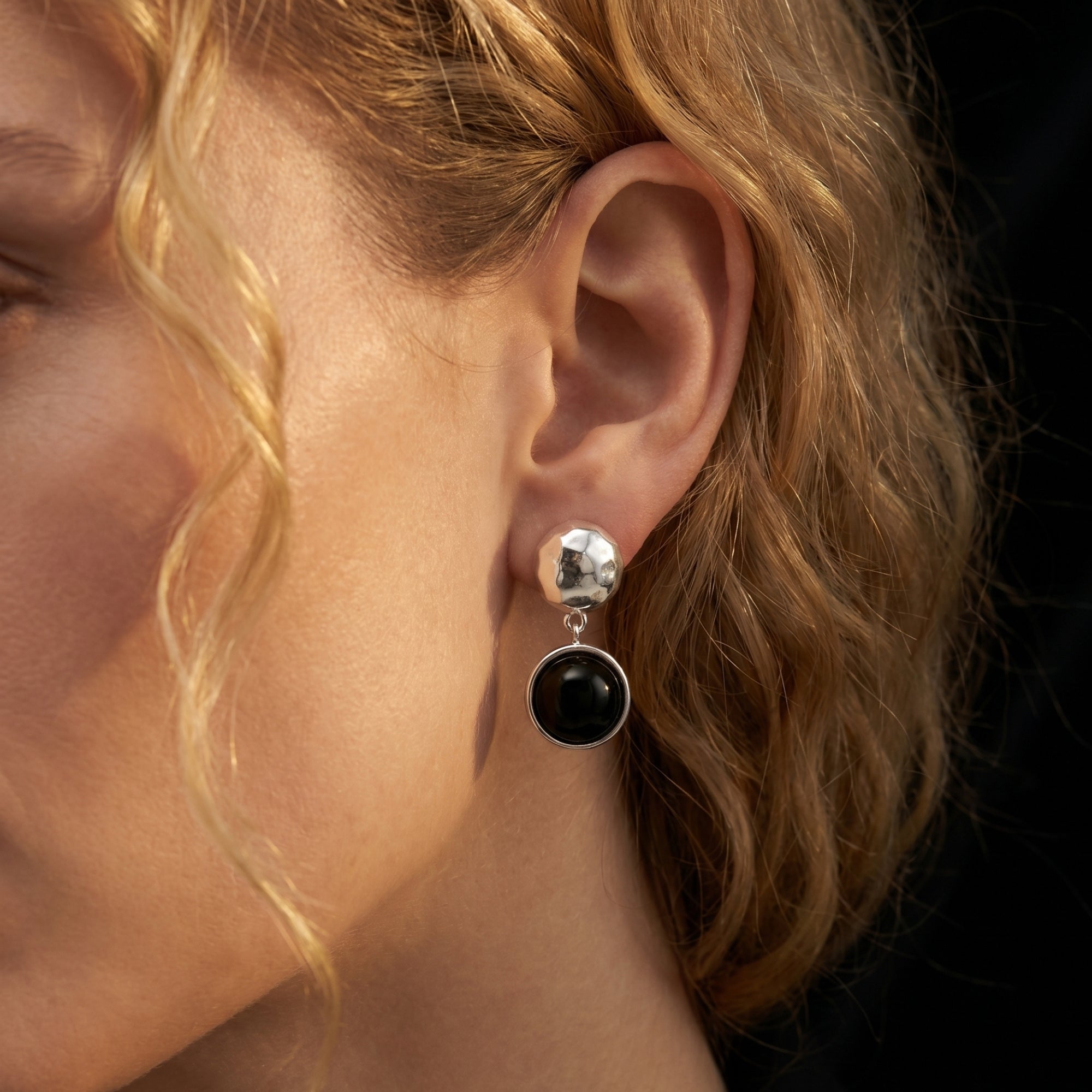 Side profile of a model wearing a Sereia silver drop earring featuring a hammered finish and round black onyx.