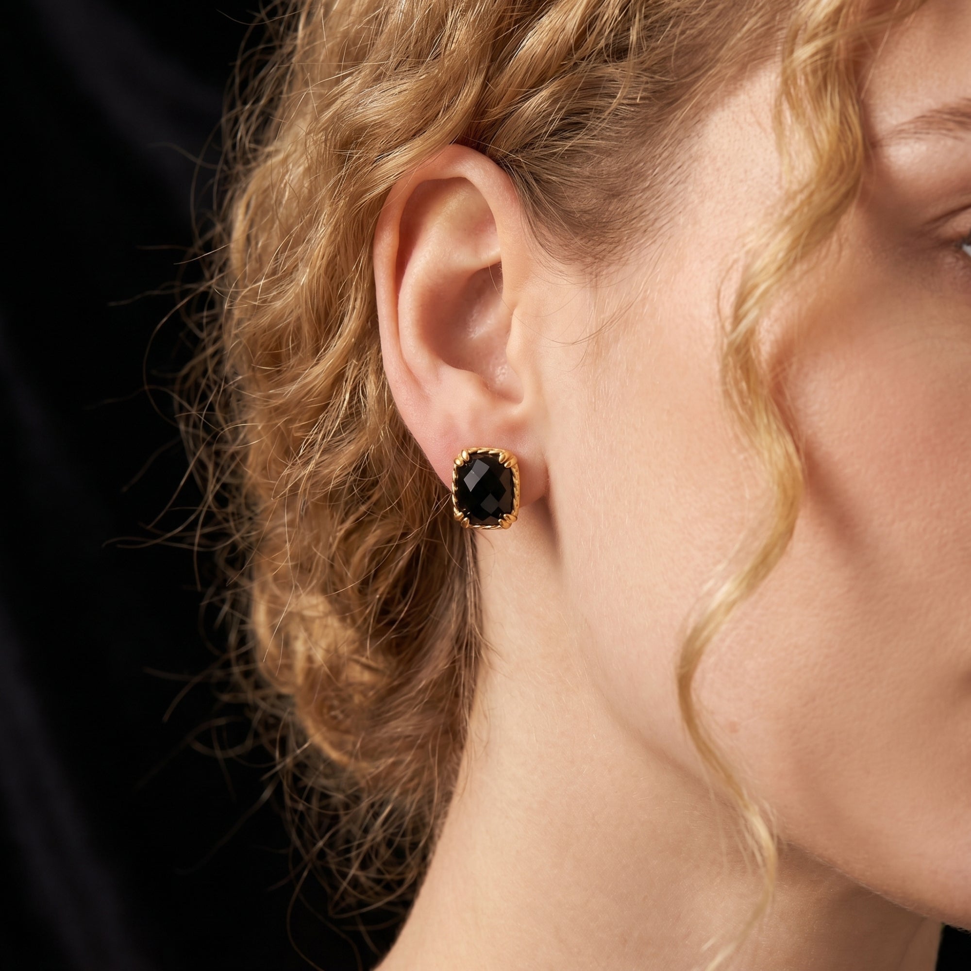 Side profile of a model wearing the gold and square-cut black onyx stud earring against a dark backdrop.