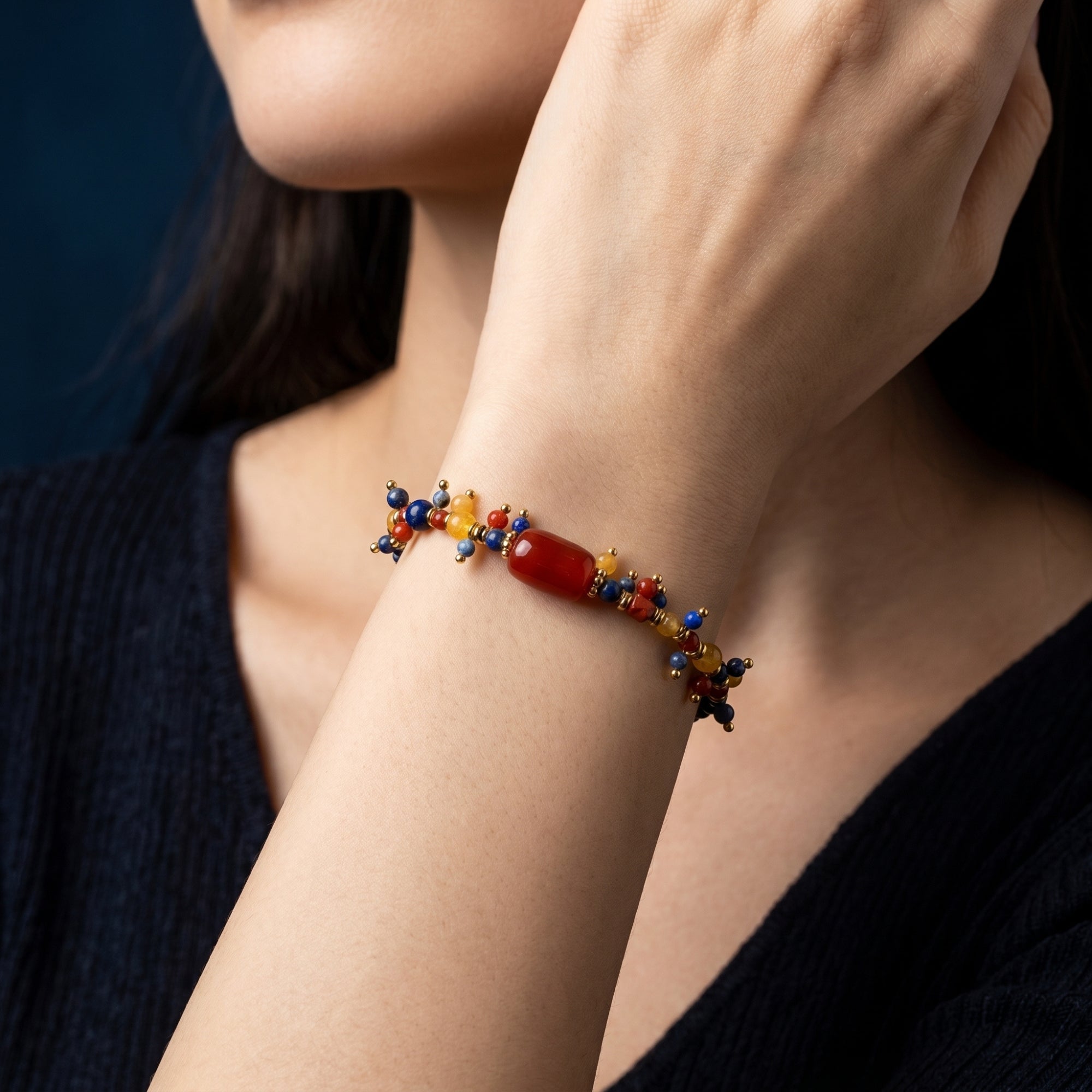 Model wearing the gold plated lapis lazuli bracelet with red and yellow beads against a dark background.