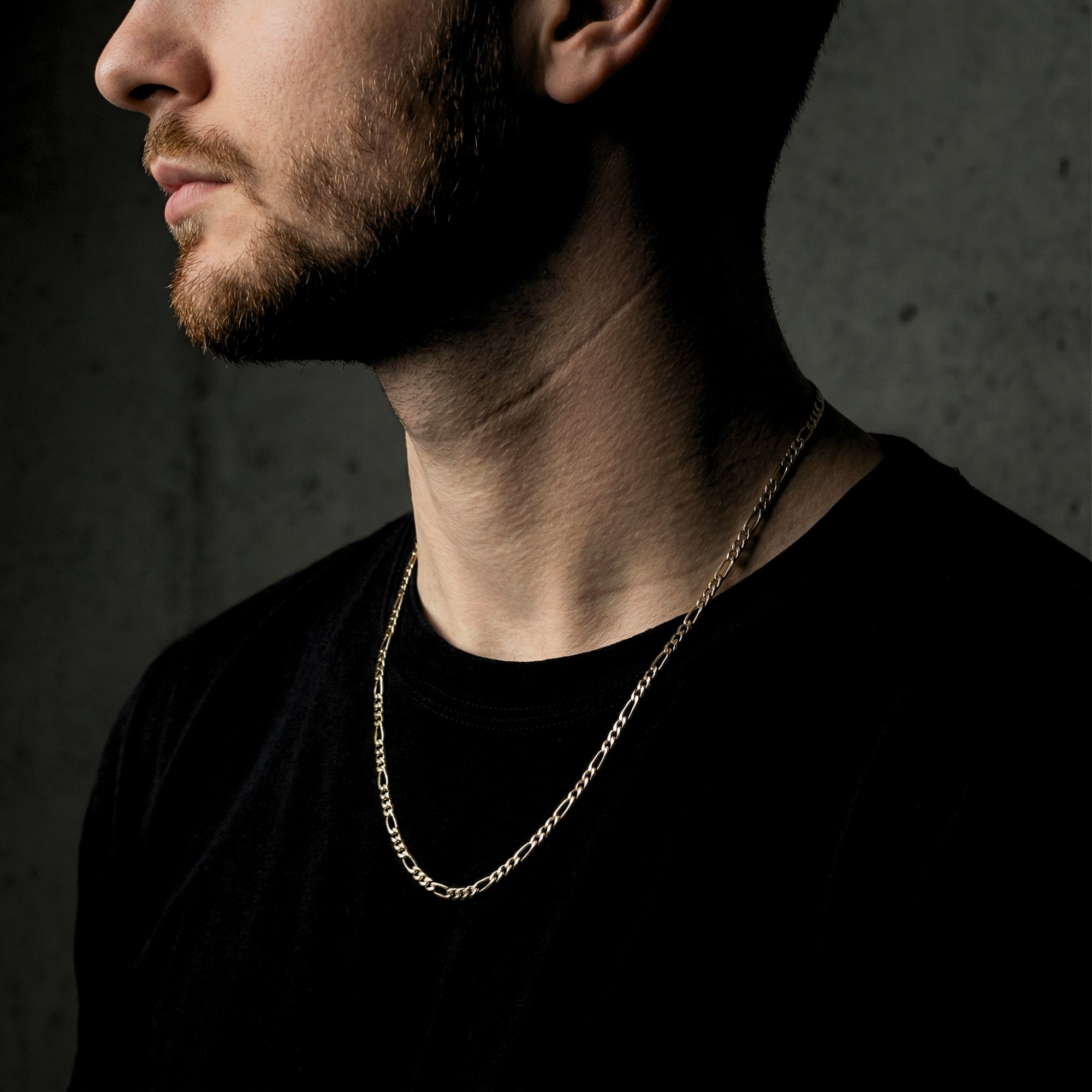 Profile view of a model wearing the gold Legacy Figaro chain against a dark background.