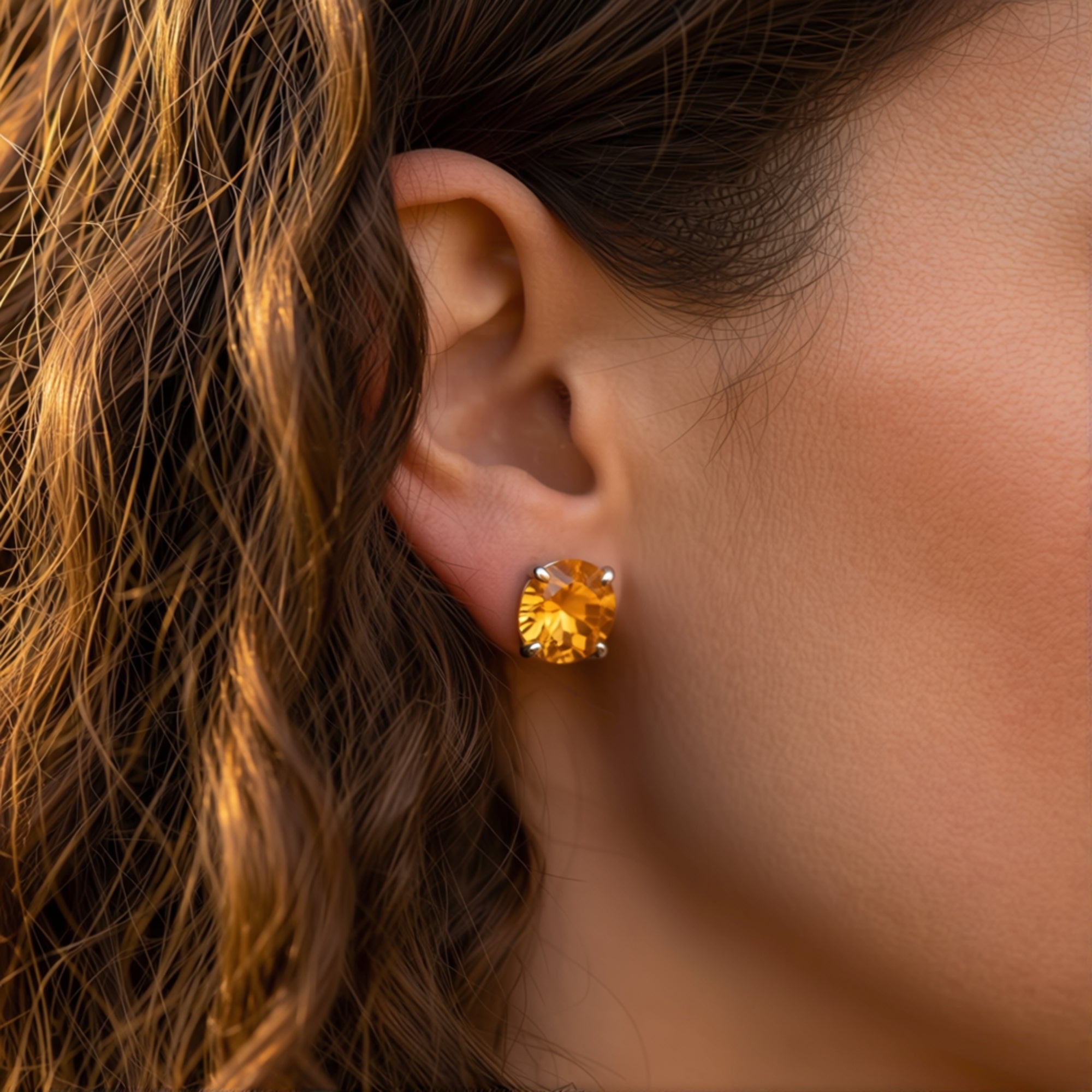 Side view of a round cut citrine earring in white gold worn on a model's ear in natural light.