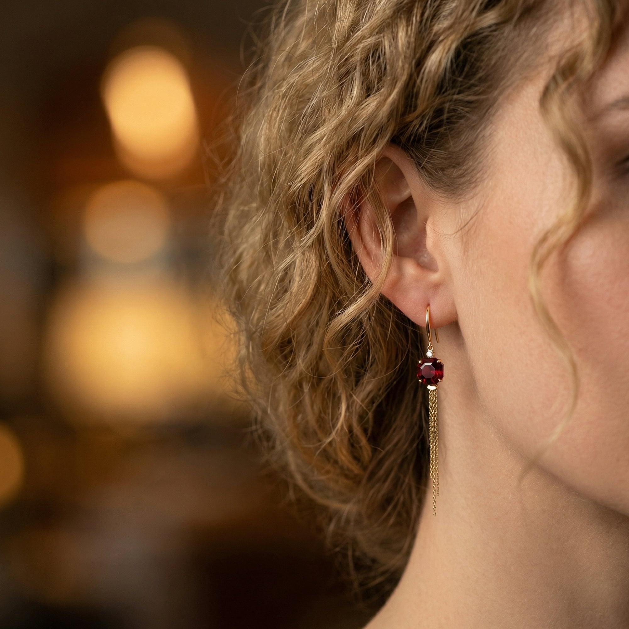 A woman wearing an 18K yellow gold drop earring featuring an octagon-cut natural red garnet and gold chains.