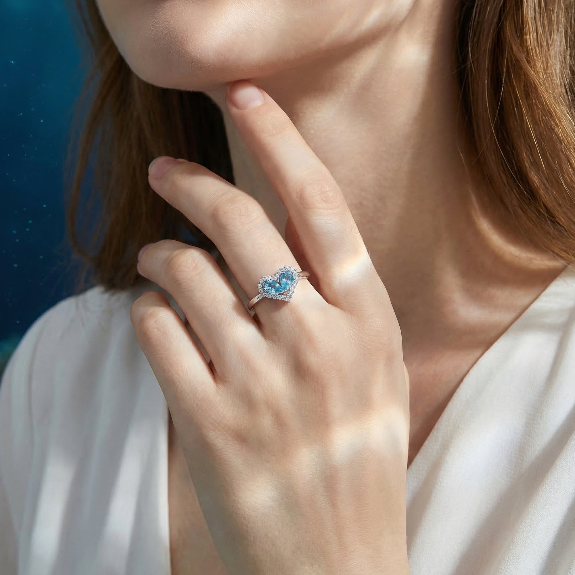 Heart-shaped aquamarine halo ring in white gold worn on a model's hand against a soft blue background.