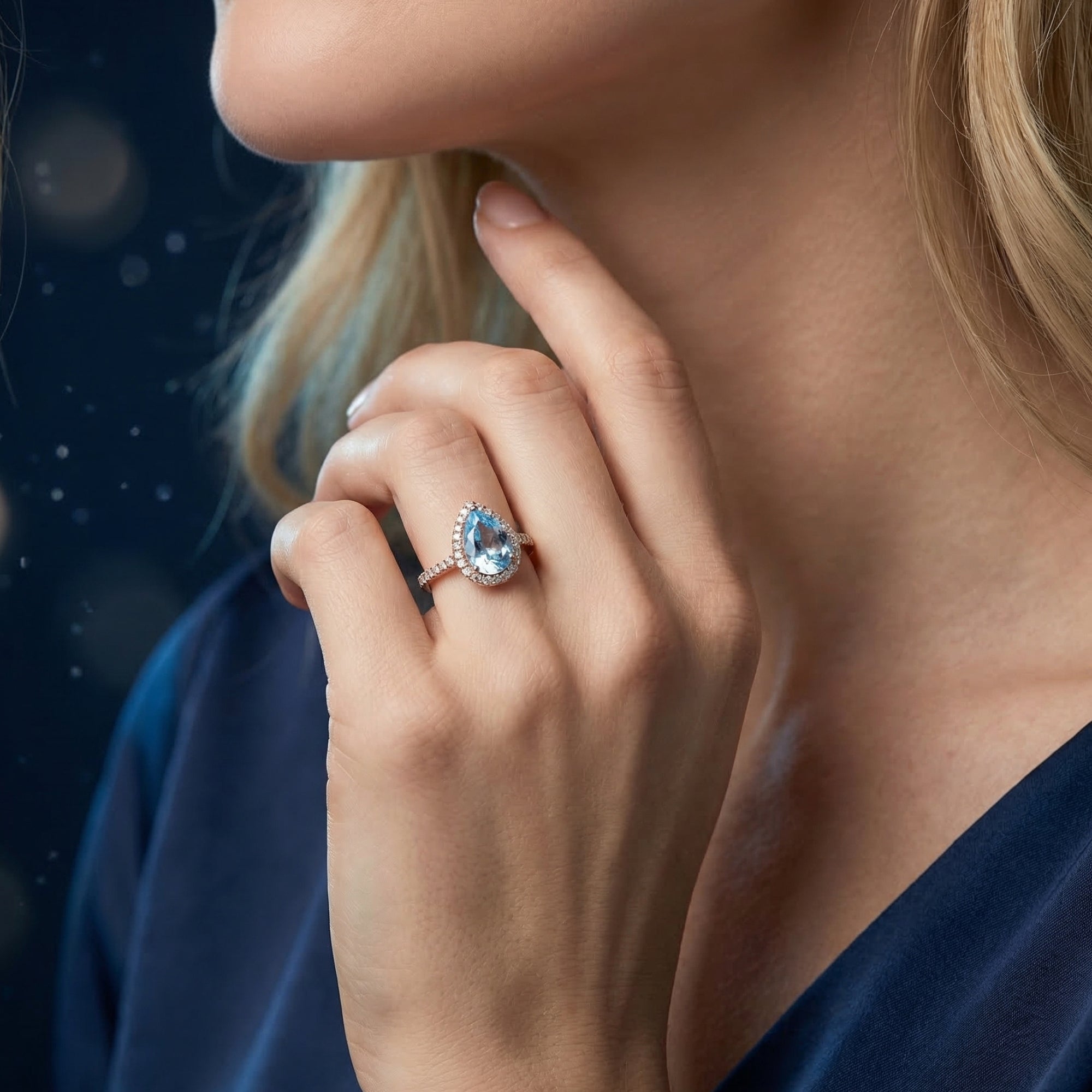 A woman wearing the pear cut blue topaz halo ring in rose gold vermeil, demonstrating its scale and sparkle.