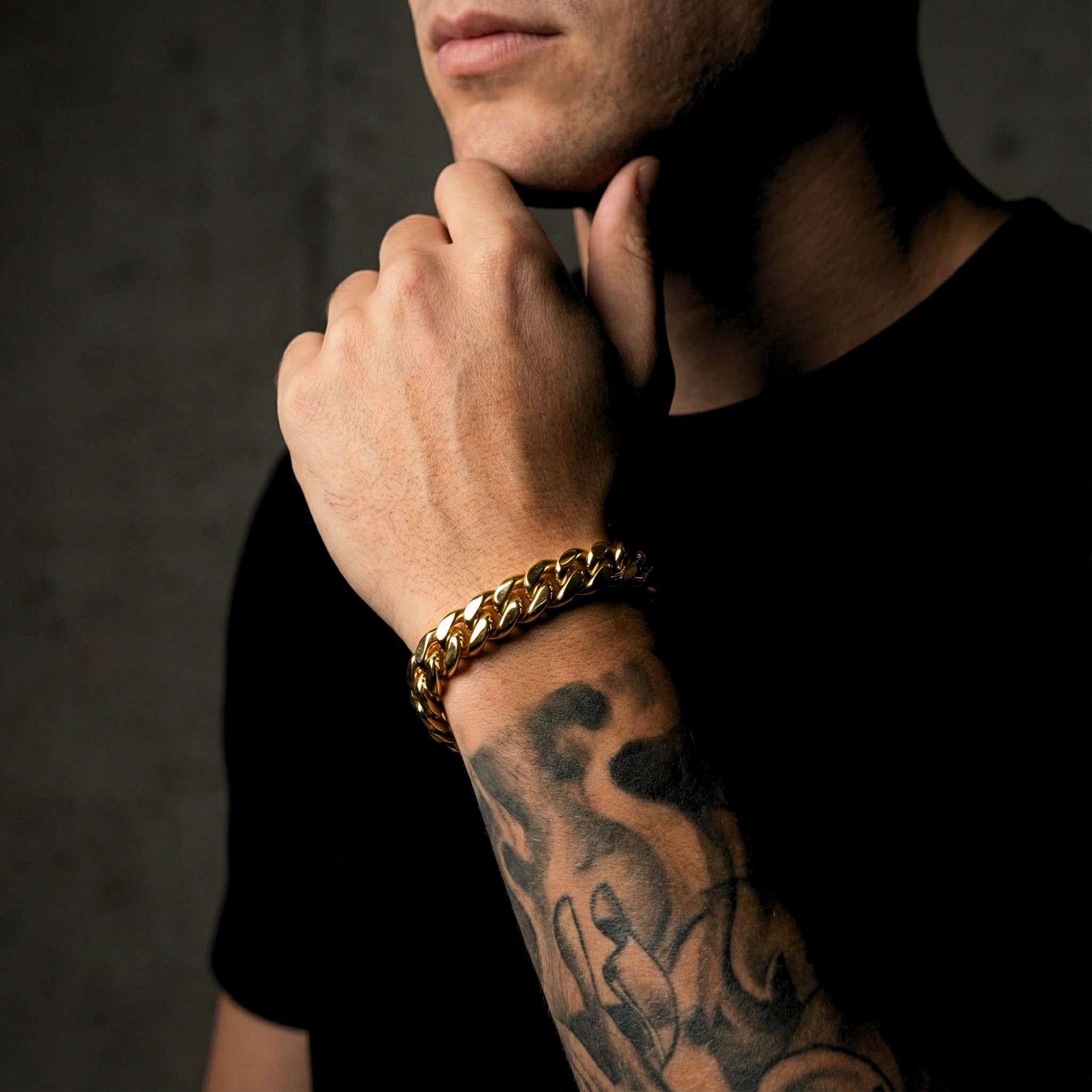 Close-up of a gold stainless steel Cuban link bracelet on a man's tattooed arm.