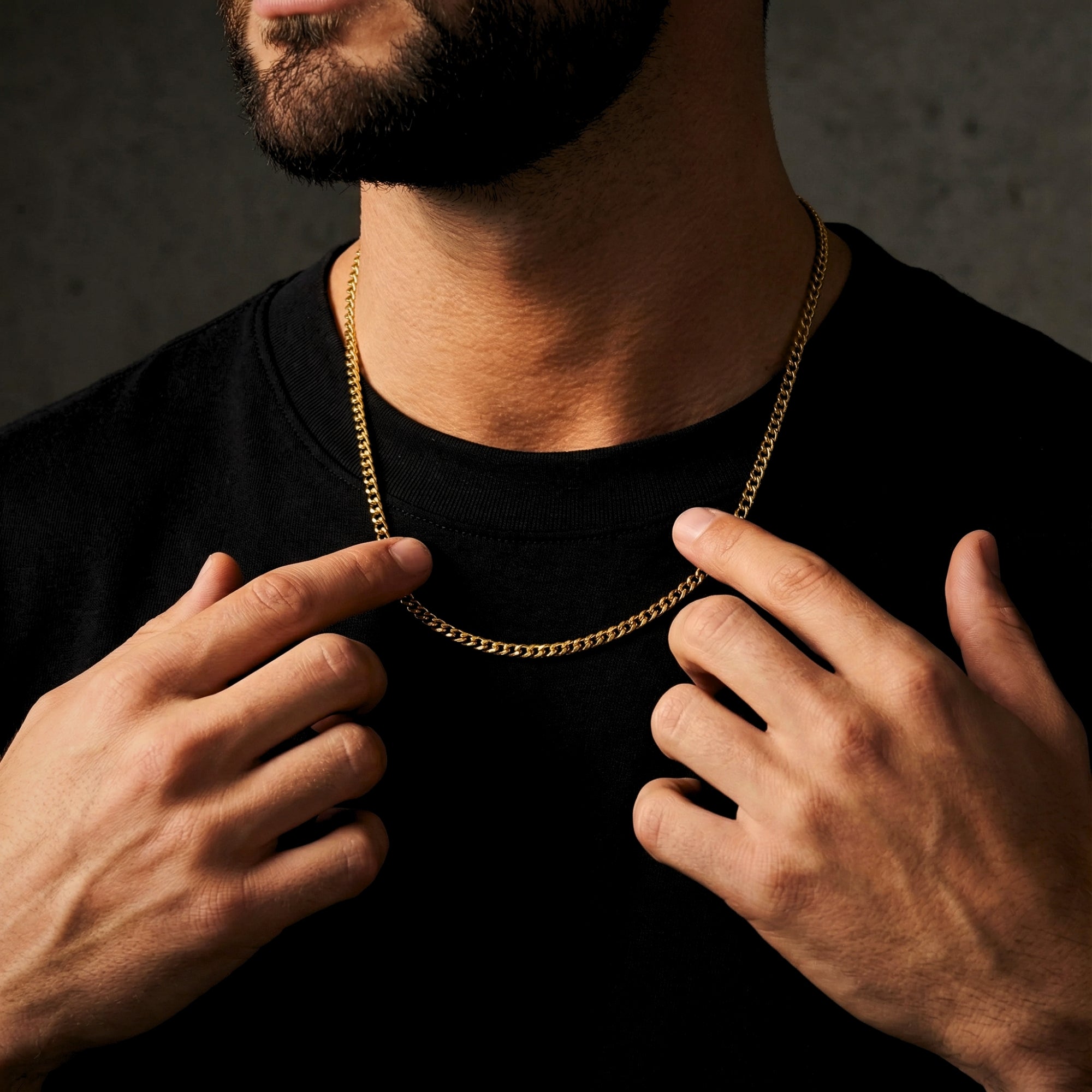 Man's hands adjusting a 4mm gold Miami Cuban link chain in stainless steel worn around the neck.
