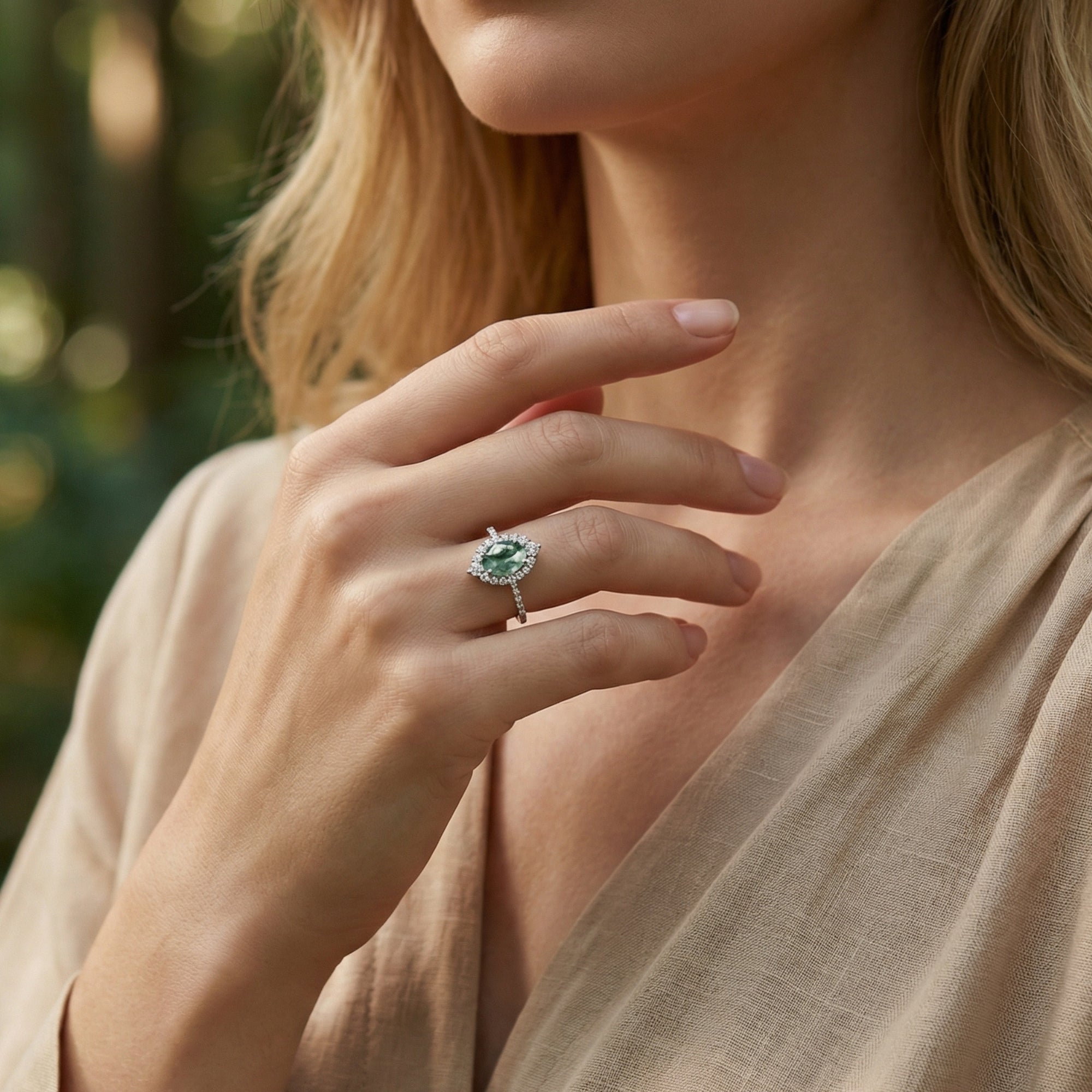 Close-up of a woman's hand wearing the oval moss agate sterling silver halo ring in a natural outdoor setting.