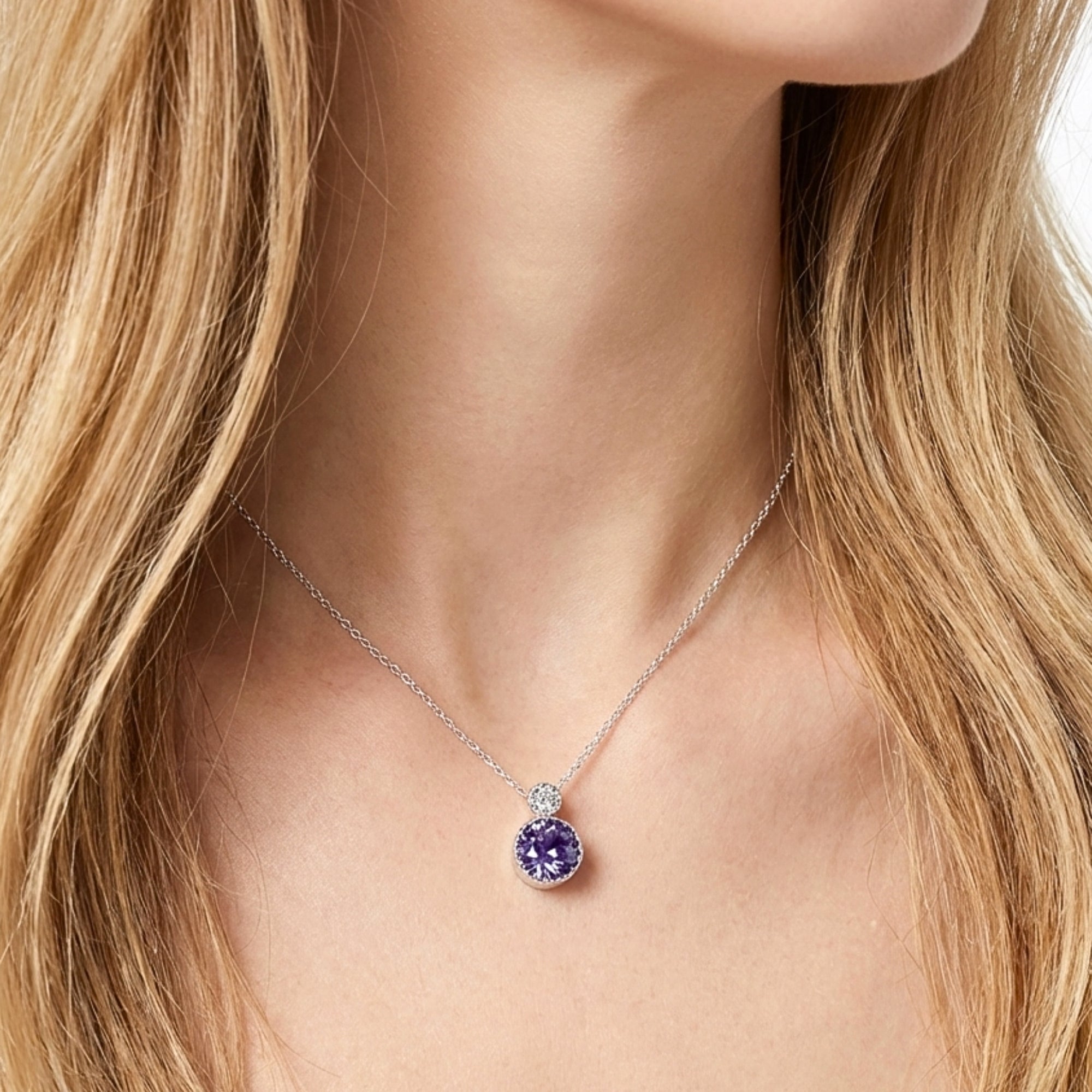 Close-up of a model wearing the round cut simulated amethyst drop necklace in silver against a white top.