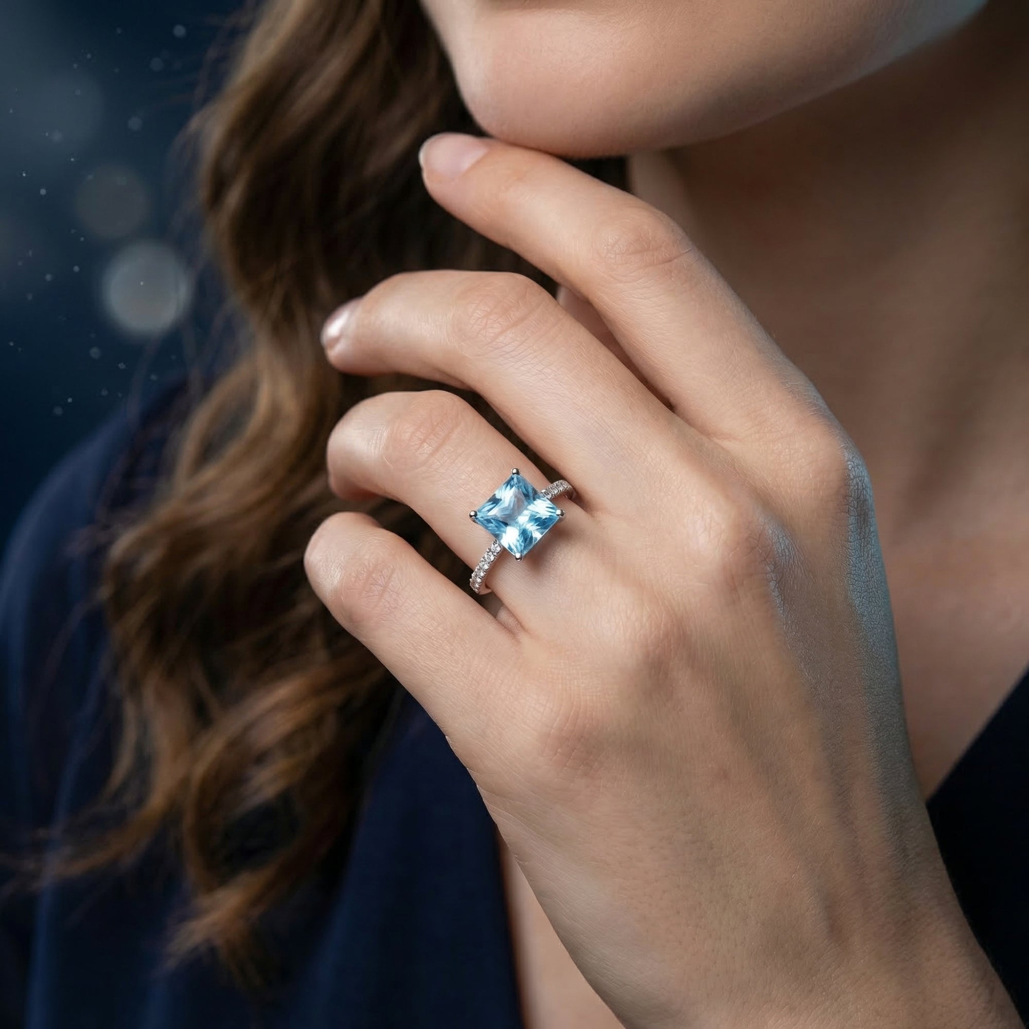 Sterling silver ring with a princess cut natural blue topaz worn by a model against a dark background.