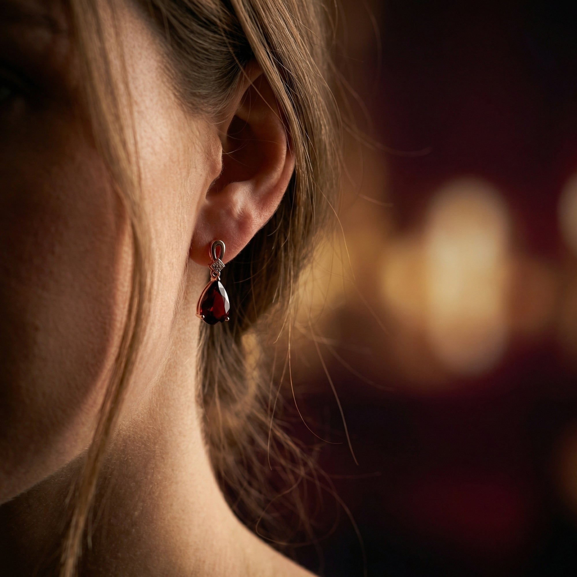 Side view of a model wearing the Odyssea 18K rose gold drop earrings with a deep red pear-cut garnet.