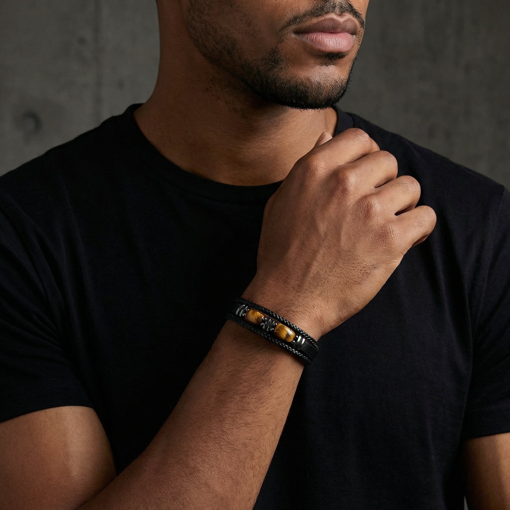 The Bastion black leather bracelet with Tiger's Eye stones and black stainless steel worn by a man in a black tee.