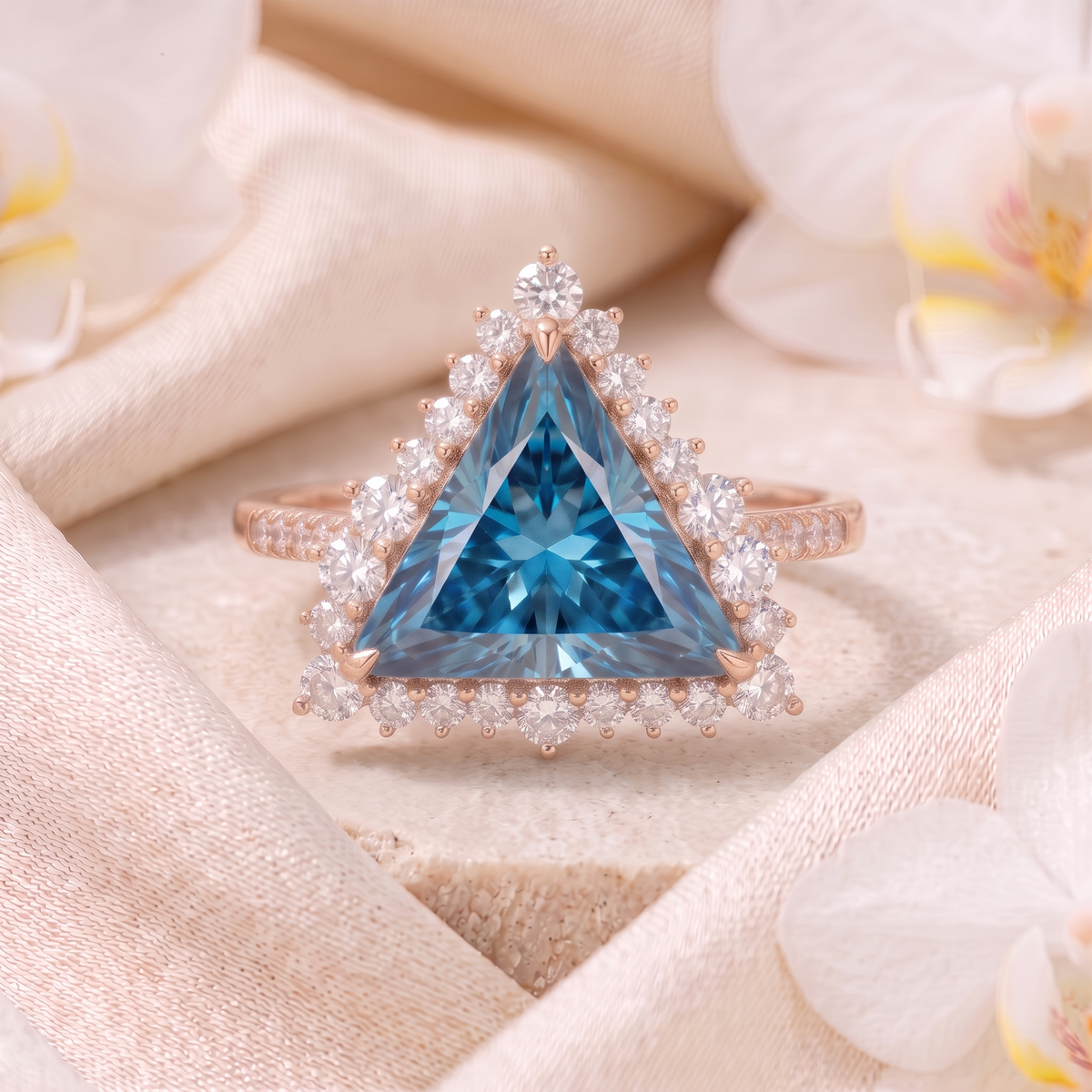 Trillion cut blue moissanite halo engagement ring in rose gold displayed on a fabric pedestal.