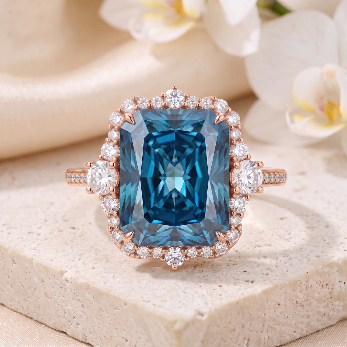 Frontal flat-lay view of a radiant cut blue moissanite halo ring in rose gold centered on a stone pedestal.