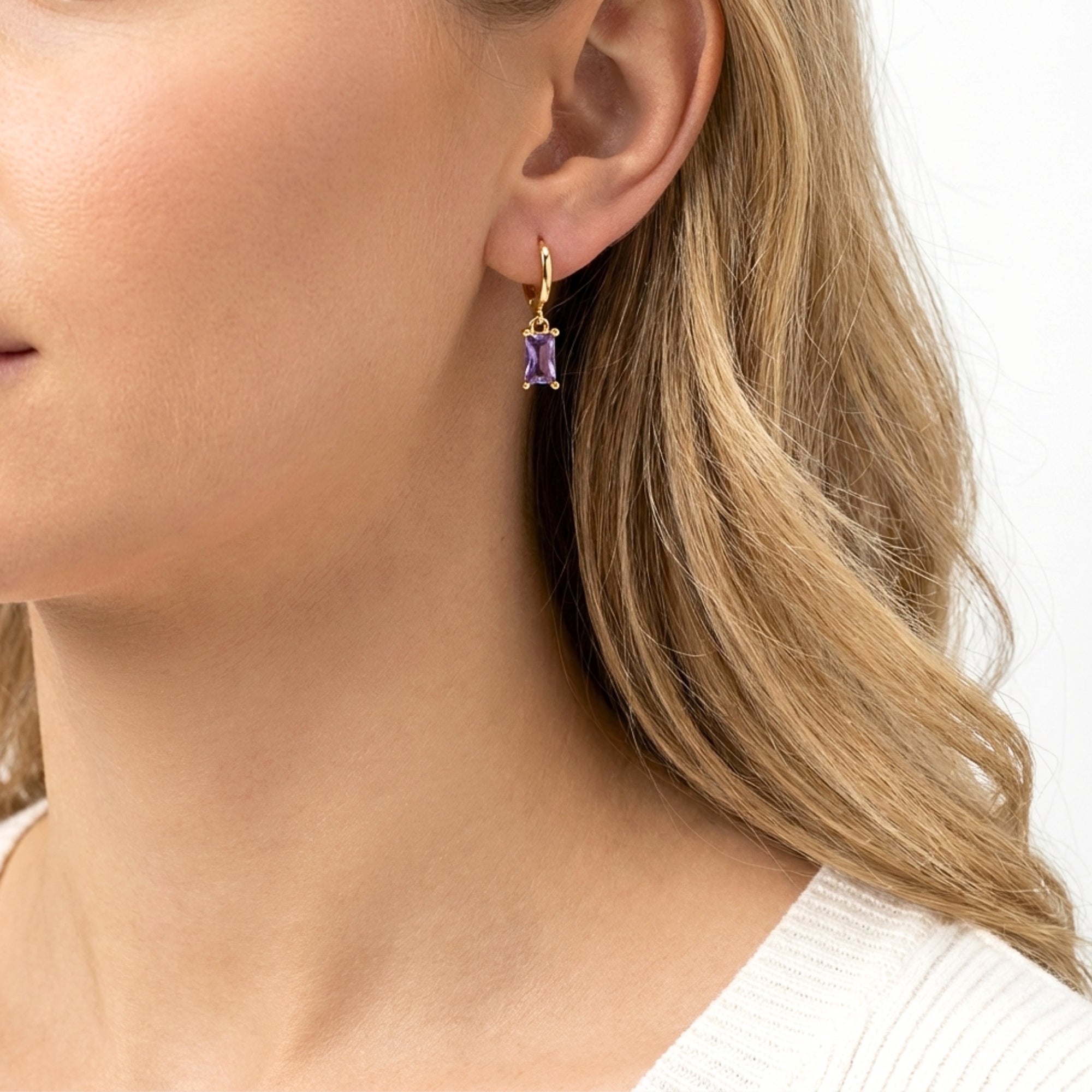 Side profile of a model wearing gold Vivienne hoop earrings with emerald cut purple simulated amethyst.