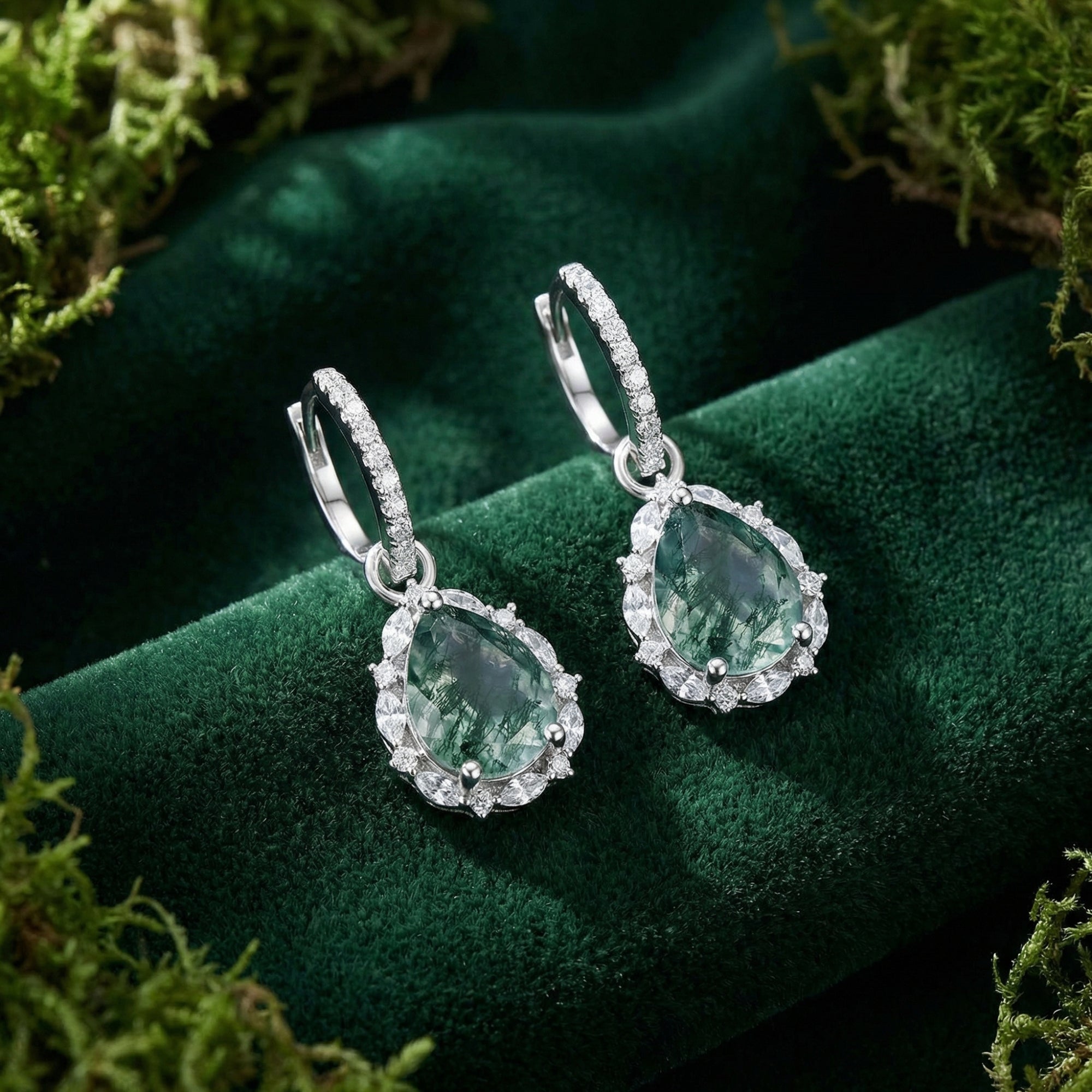 Pair of pear-cut Moss Agate drop earrings in sterling silver halo settings displayed on green velvet.