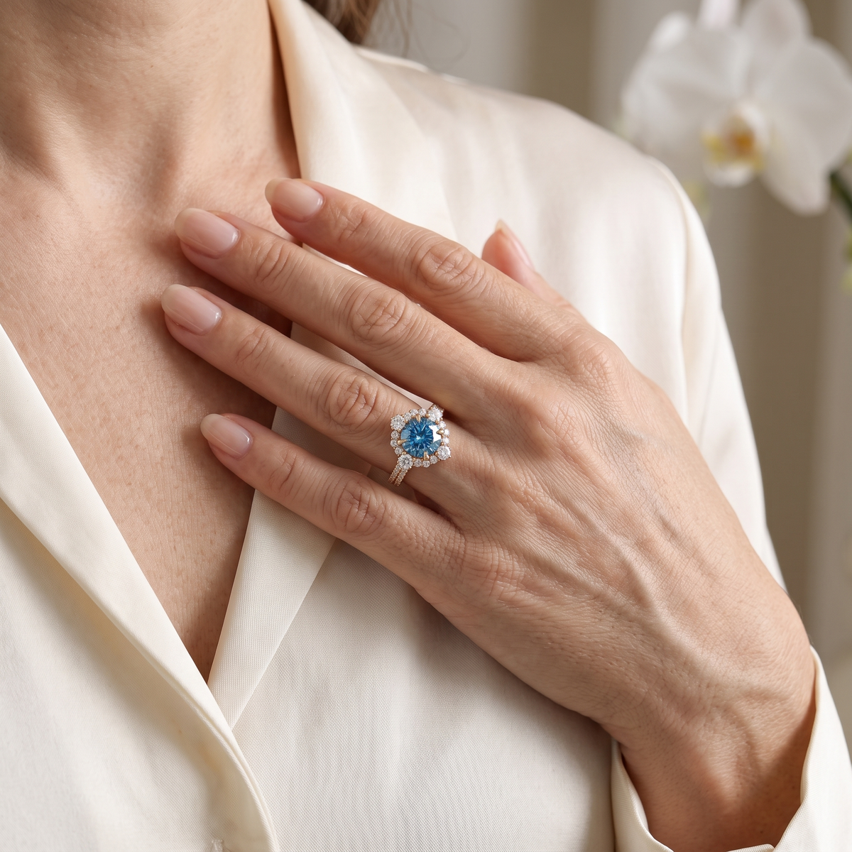 A model wearing a rose gold ring with a blue moissanite center stone held near her collarbone.