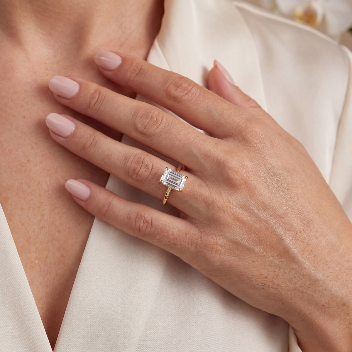 A woman wearing a yellow gold solitaire ring featuring a large emerald-cut moissanite.