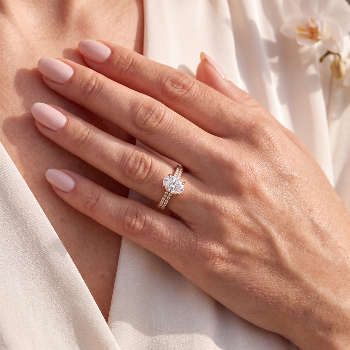 Close-up of model wearing gold oval moissanite engagement ring with double-row pavé band.