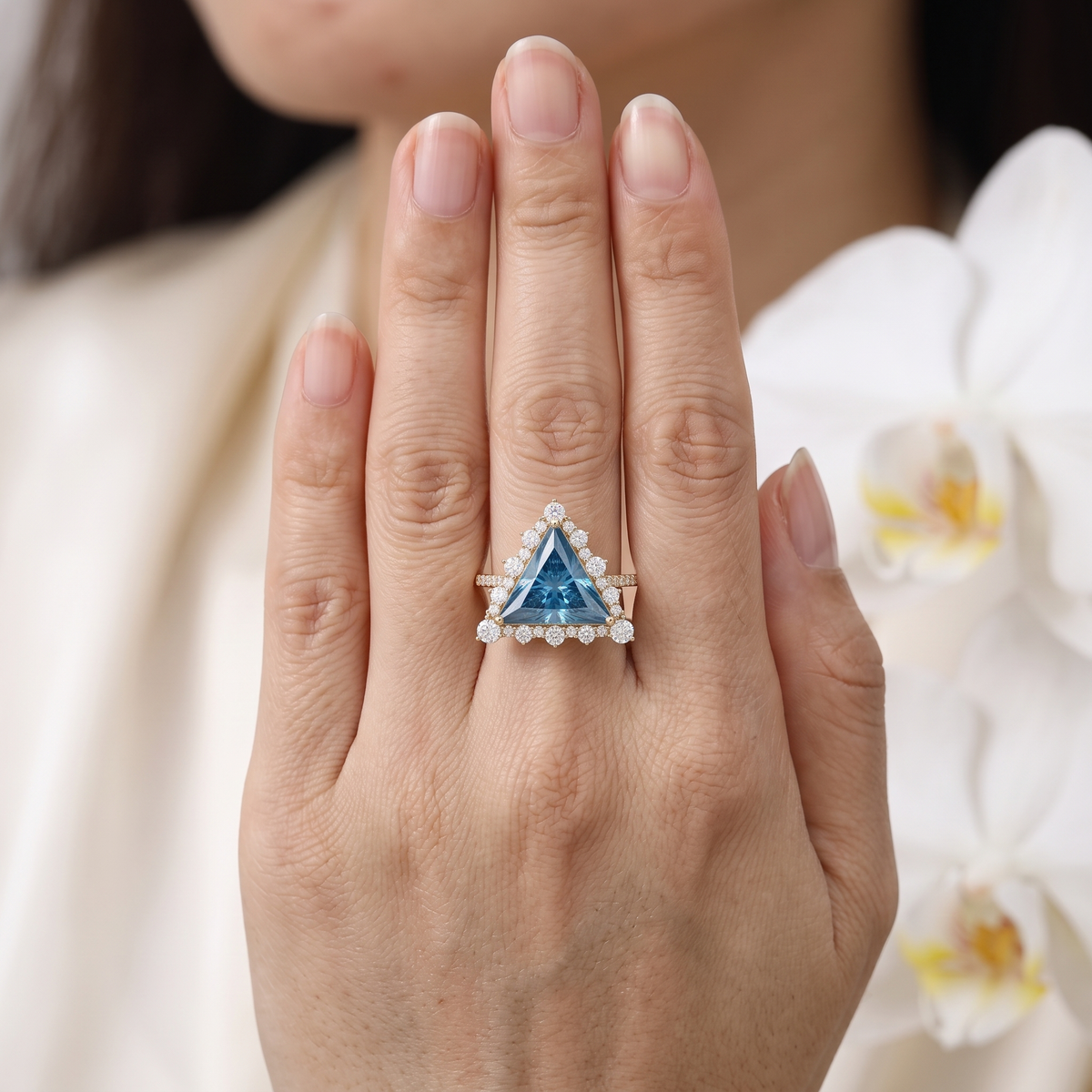 Front-facing view of a trillion cut blue moissanite halo ring in rose gold displayed on a stone surface.