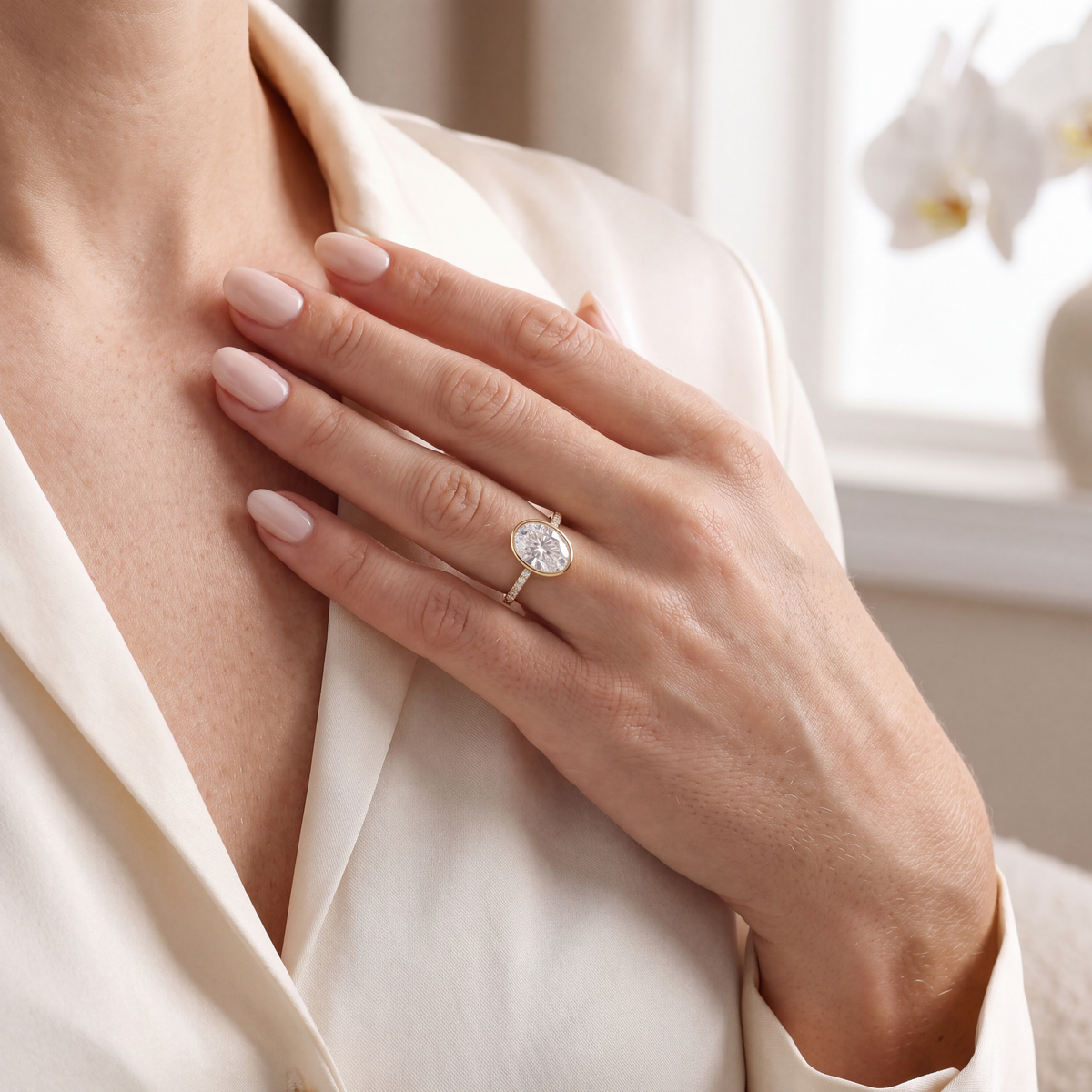 Yellow gold oval moissanite bezel ring styled on a model wearing a white silk blouse.
