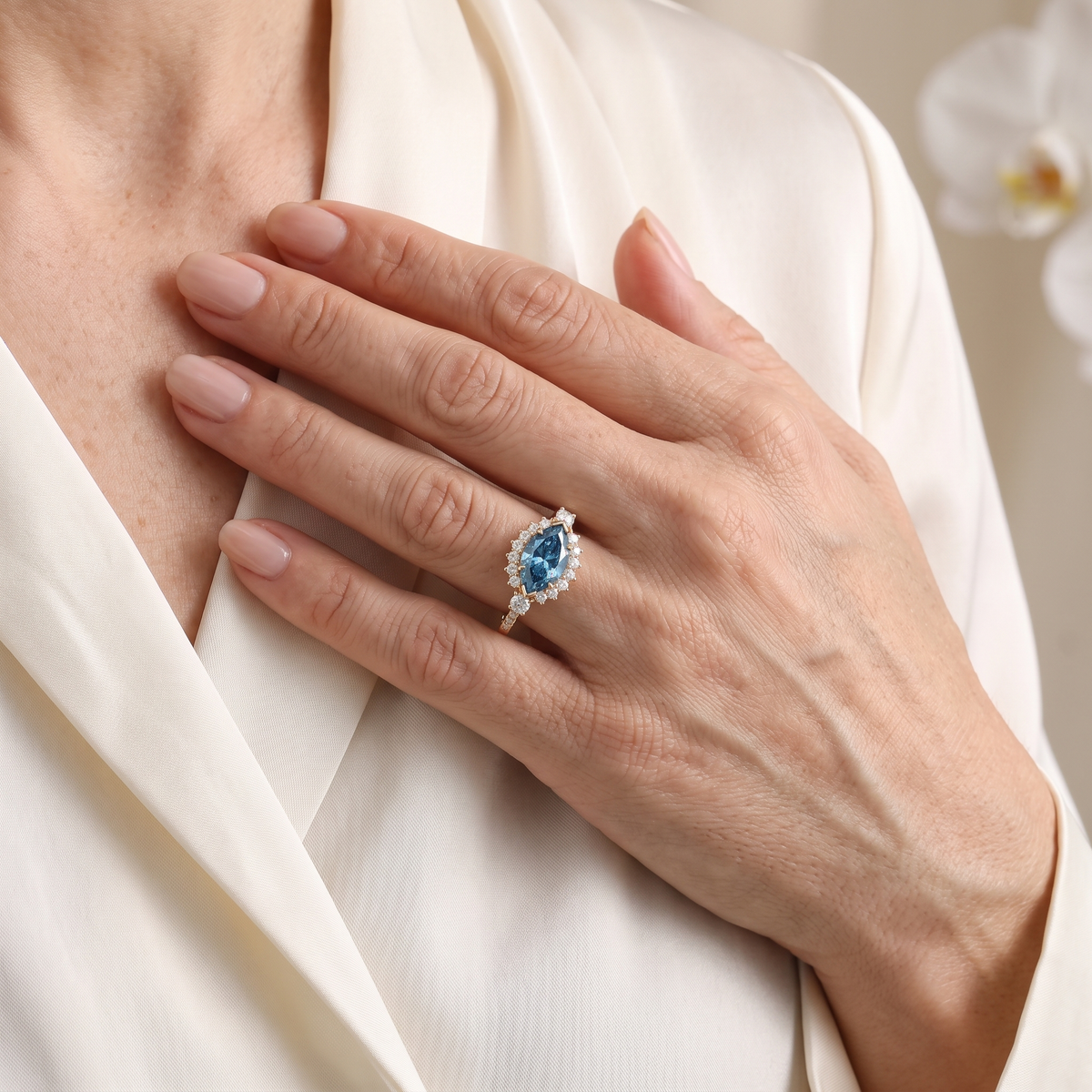 Model with hand resting on chest wearing an elegant rose gold marquise blue moissanite halo ring.