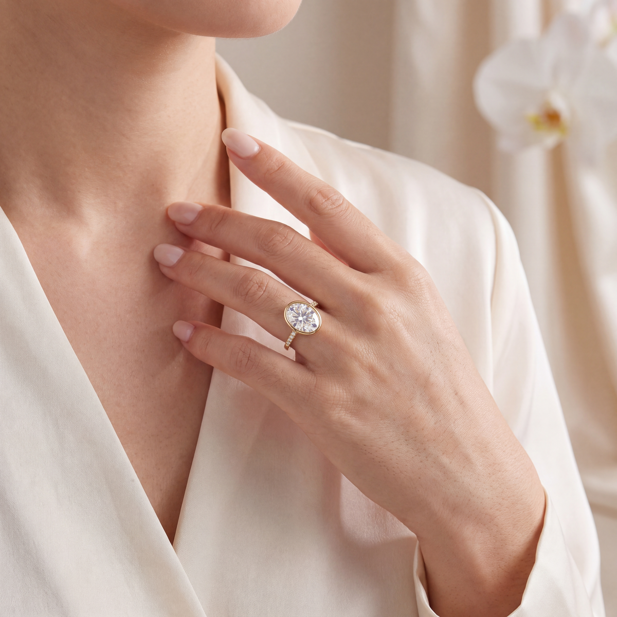 Model holding her hand near her chest showcasing the yellow gold oval moissanite bezel ring.