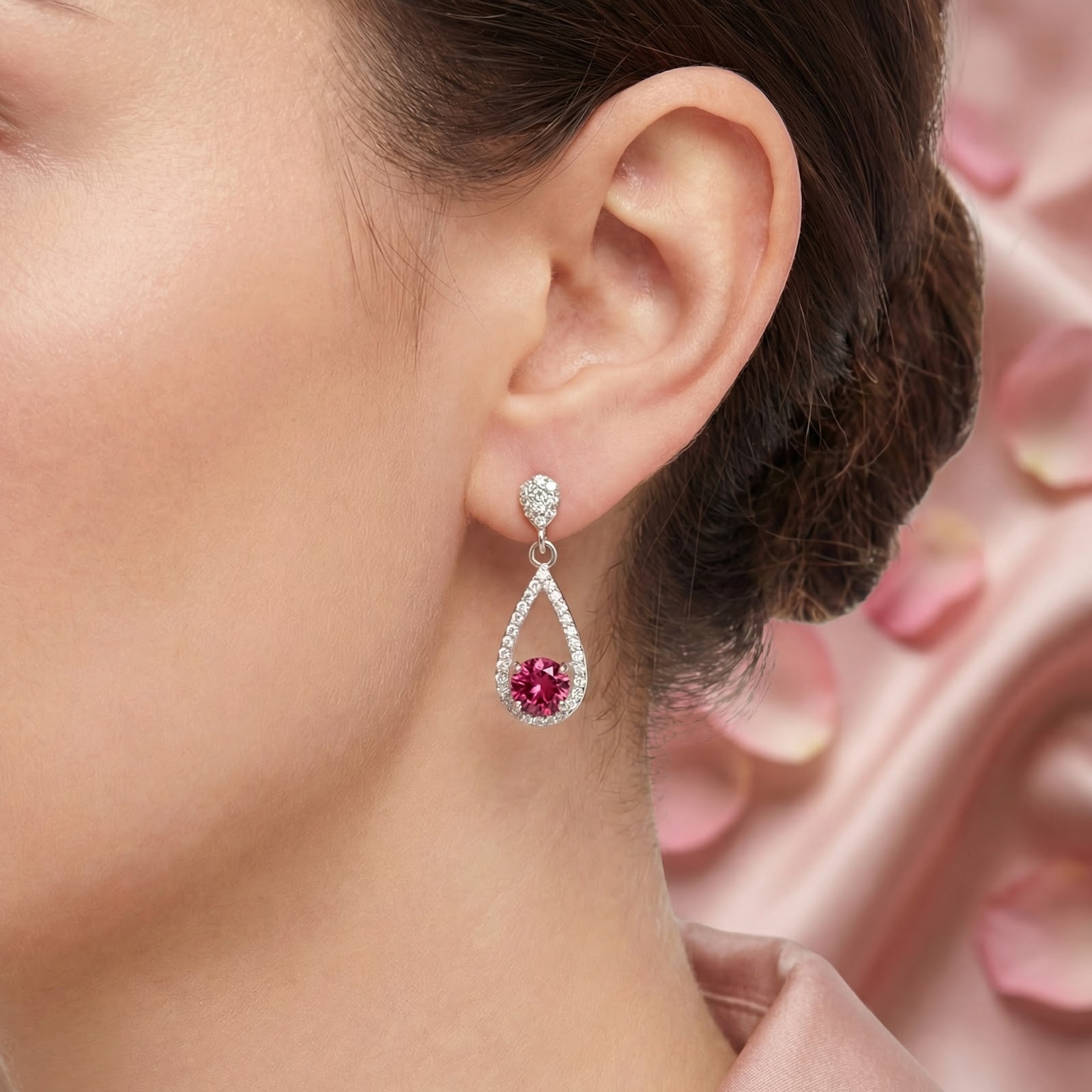 Close-up of a sterling silver teardrop earring with a round pink tourmaline stone on a woman's ear.
