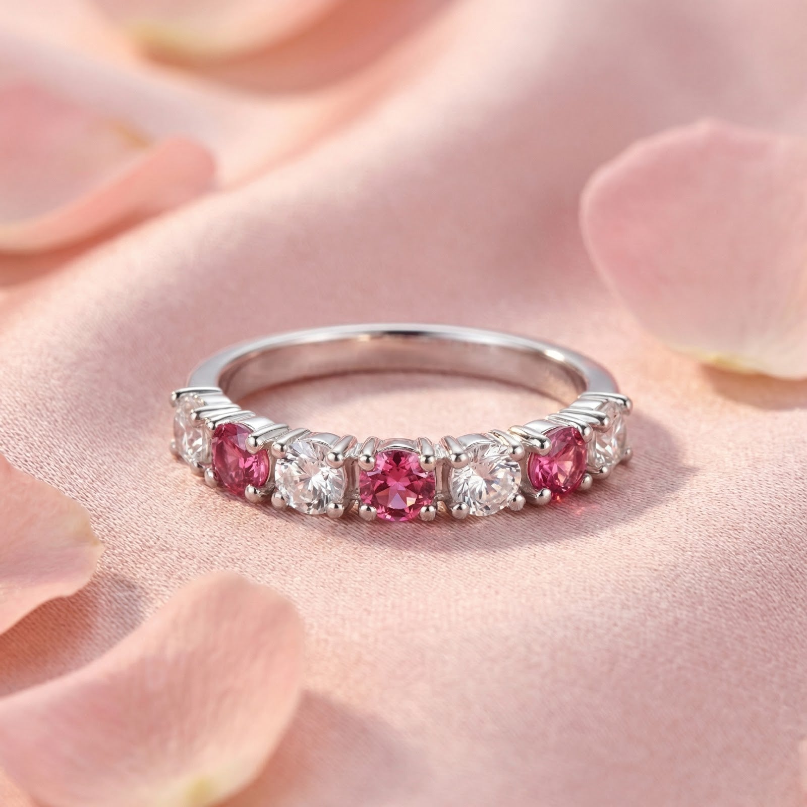 Sterling silver pink tourmaline and clear stone ring displayed on pink fabric with scattered rose petals.