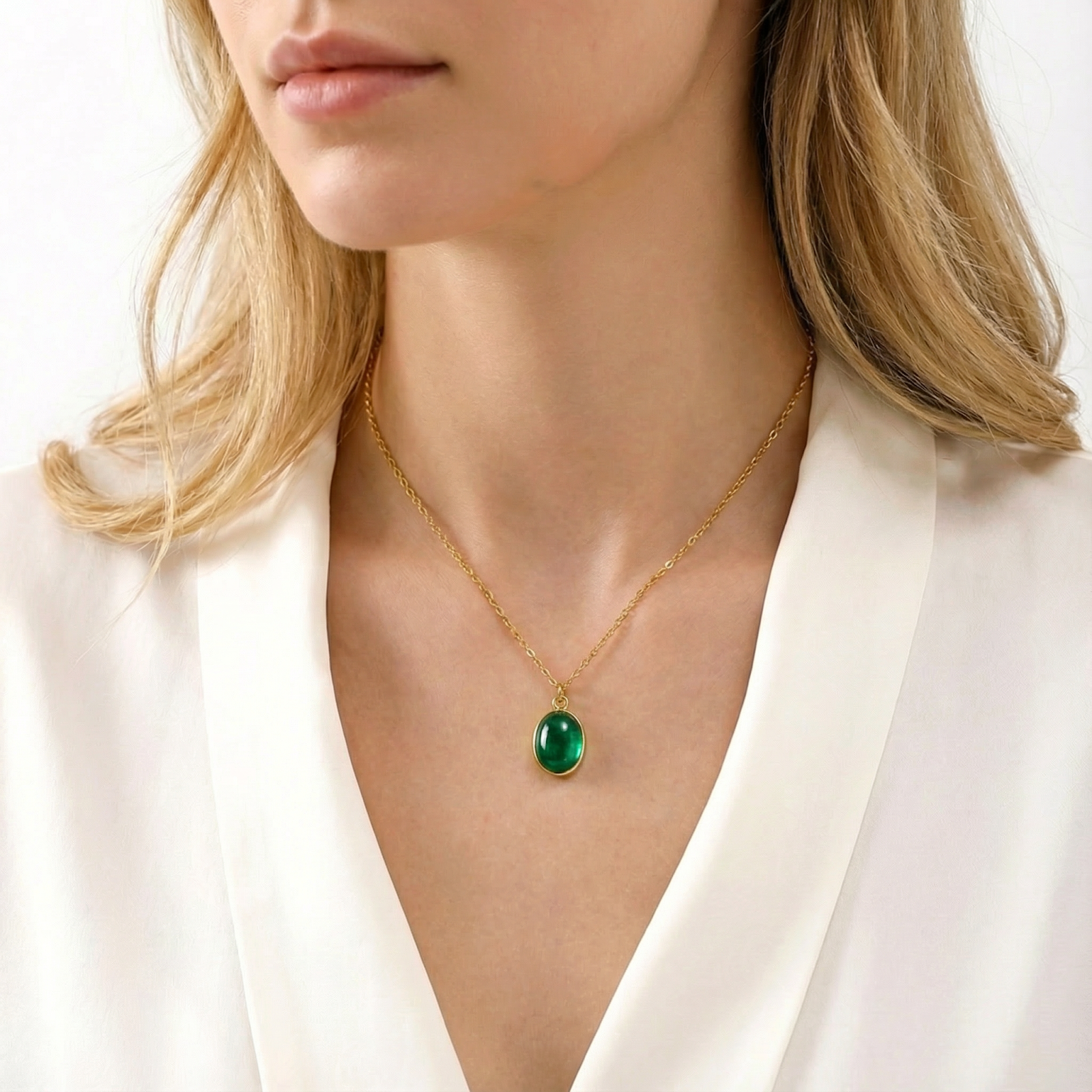 Gold-finished stainless steel teardrop necklace with a green simulated emerald worn by a model on a white blouse.